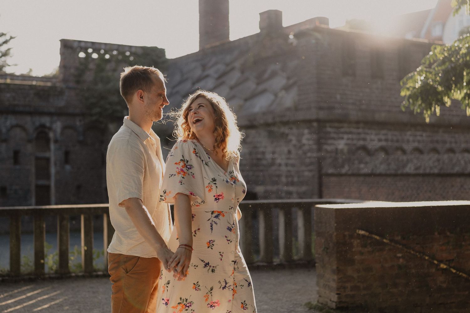 Couple embracing in warm sunlight against rustic brick wall backdrop.