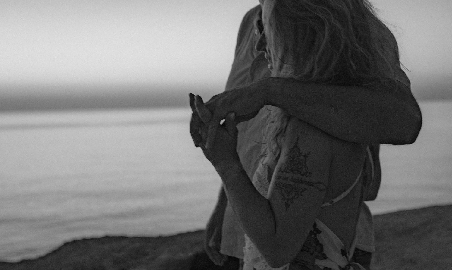 Black and white photo of couple in intimate embrace by the ocean.