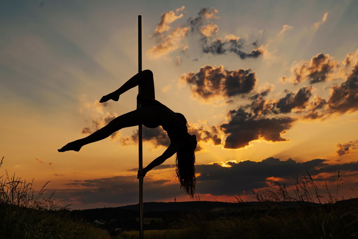 Silhouette of a woman pole dancing against a dramatic golden sunset sky with clouds.