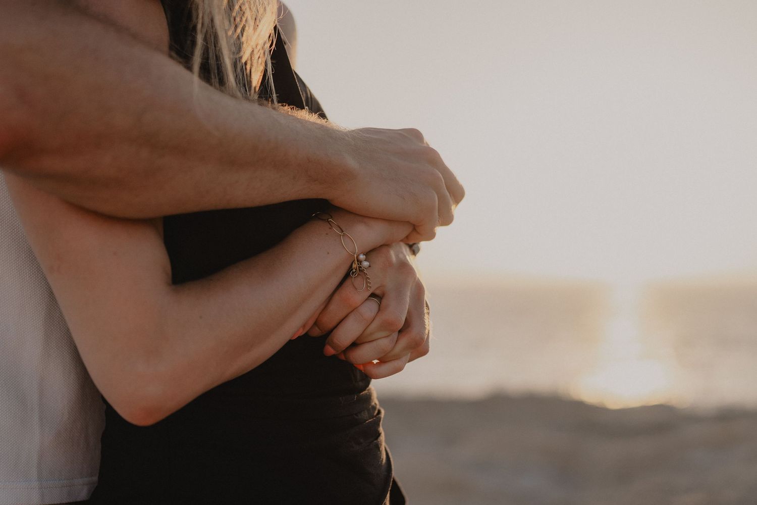 Couple embracing at sunset on a beach, woman wearing a ring, romantic golden hour photography.