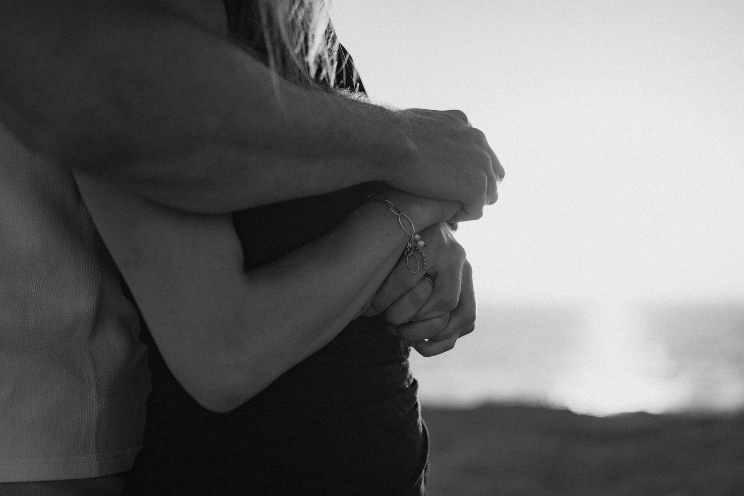 Black and white photo of a couple embracing tenderly, with the ocean visible in the background.