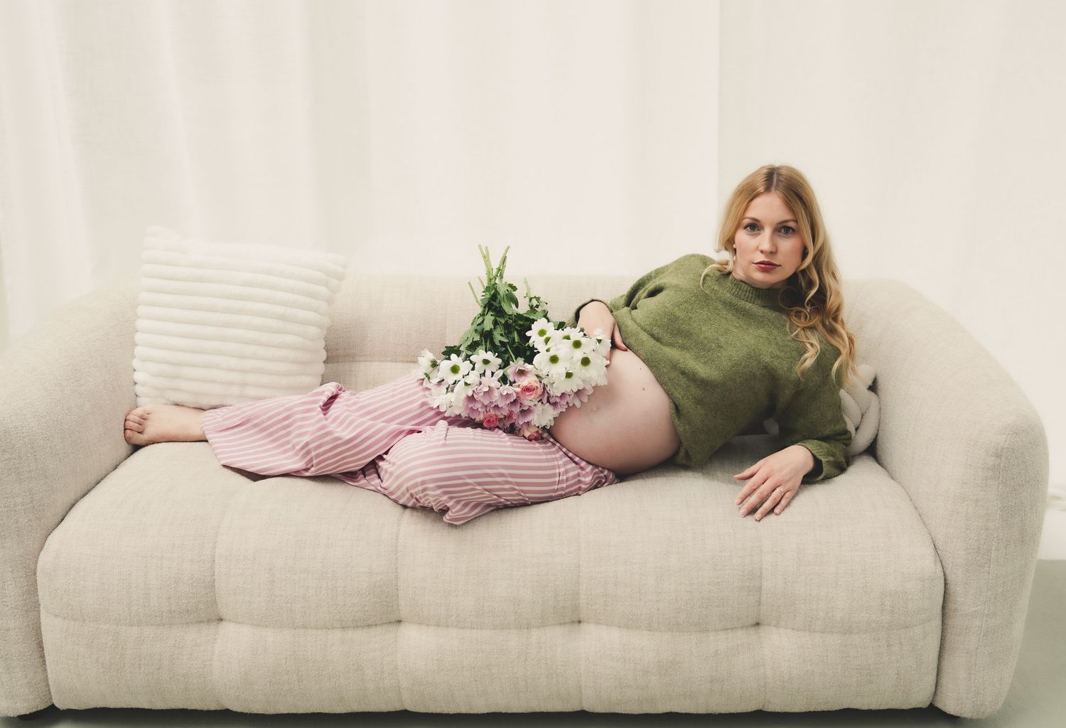 Woman in green sweater and pink pants relaxing on beige sofa with white flowers.