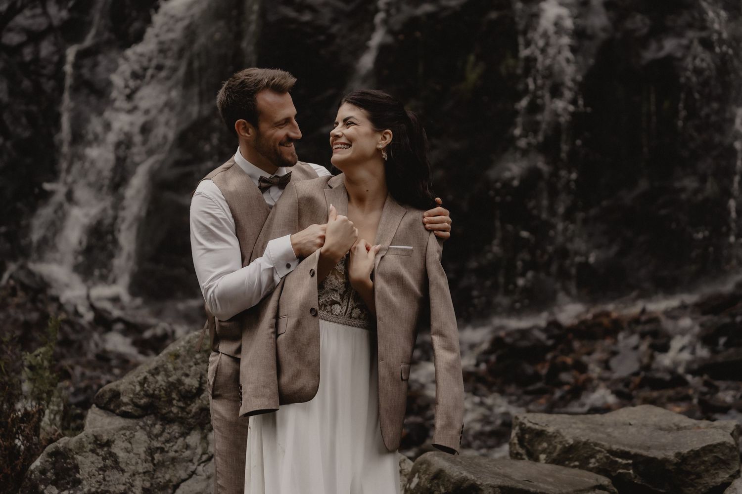 Joyful wedding moment captured against dramatic waterfall backdrop.