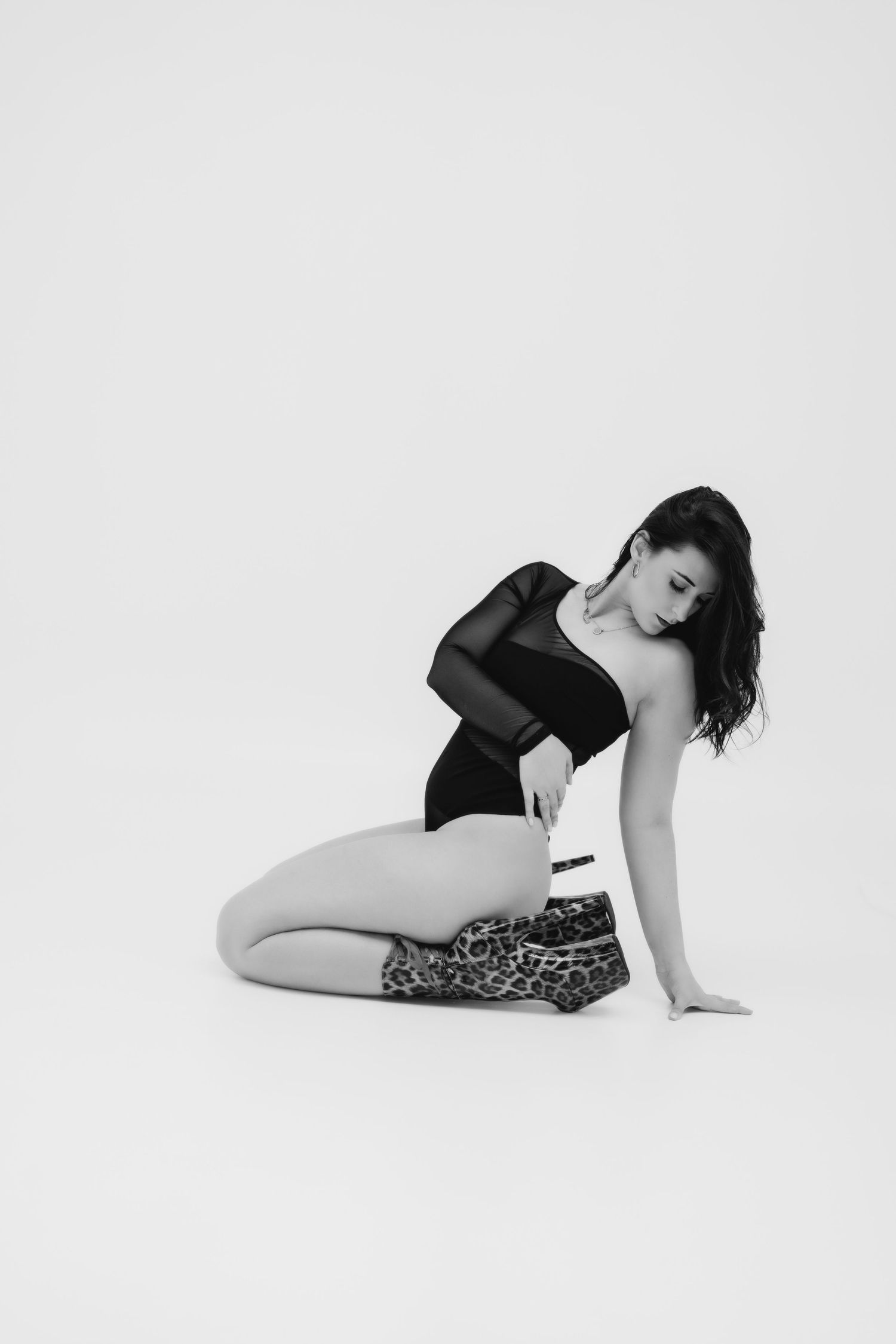 Black and white studio shot of woman in black bodysuit with leopard print heels posing.