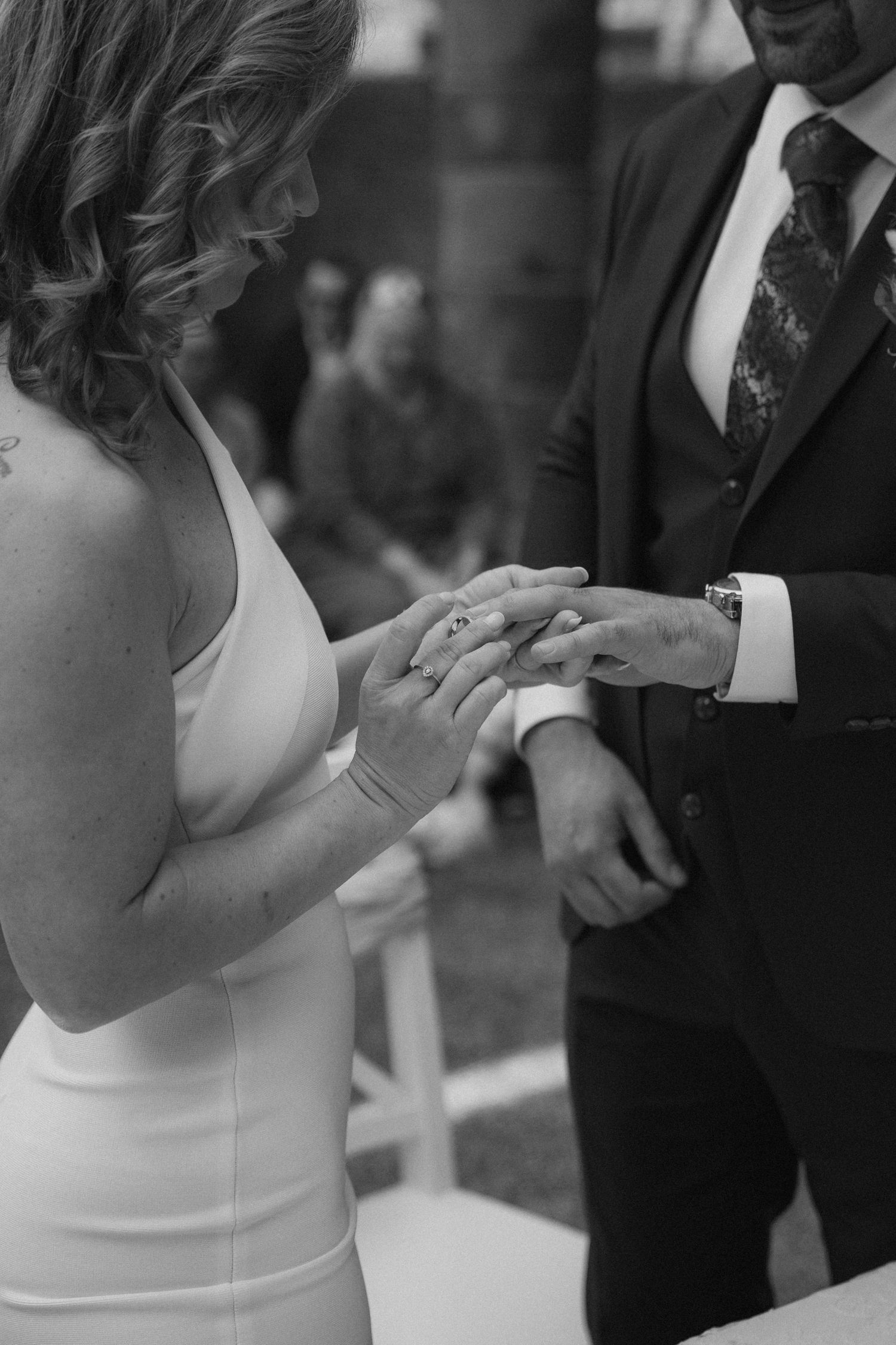 A close-up black and white photo of hands exchanging wedding rings during a ceremony.