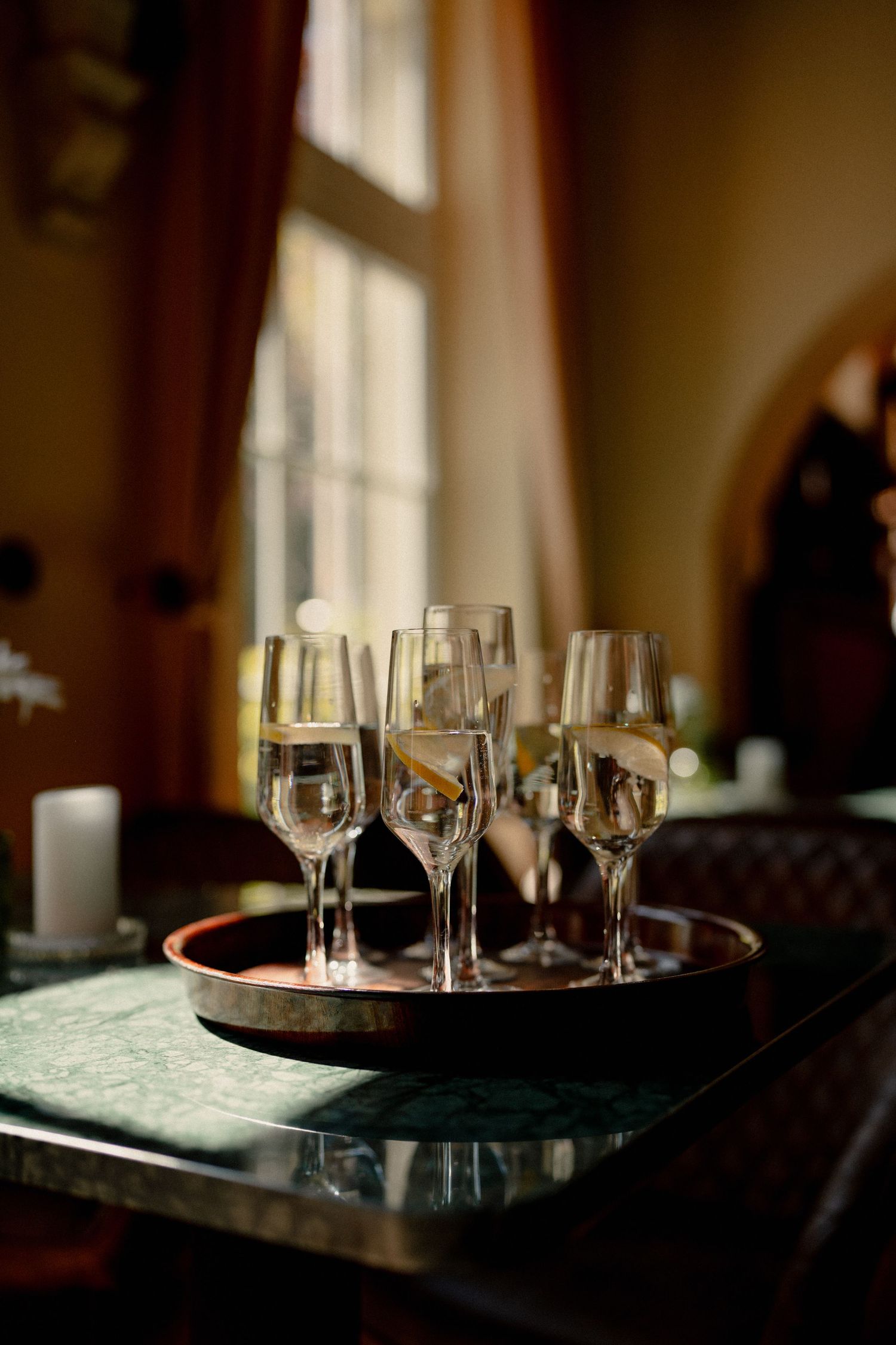 Elegant champagne flutes filled with sparkling wine arranged on a round tray by a window.