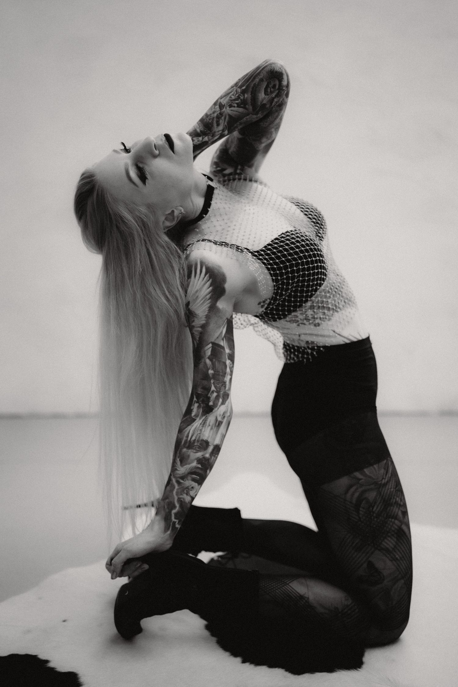 Black and white artistic photo of a woman in polka dot top and dark pants posing with dramatic backbend on snowy ground.