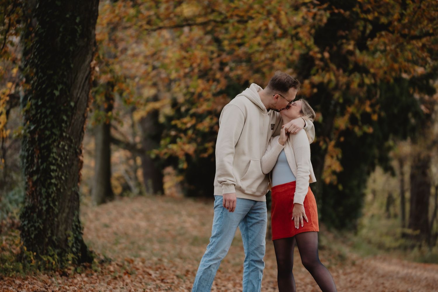 A romantic couple sharing an intimate moment in a fall forest setting with autumn leaves in the background.
