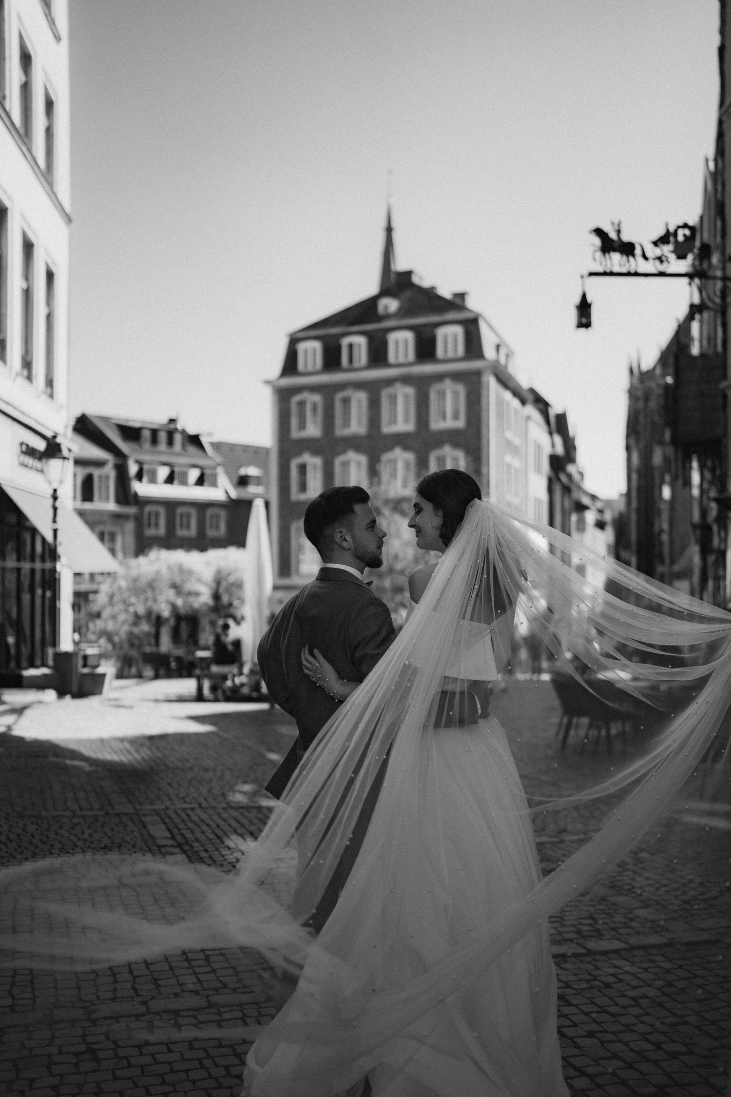 Wedding couple in black and white on cobblestone street with flowing veil.