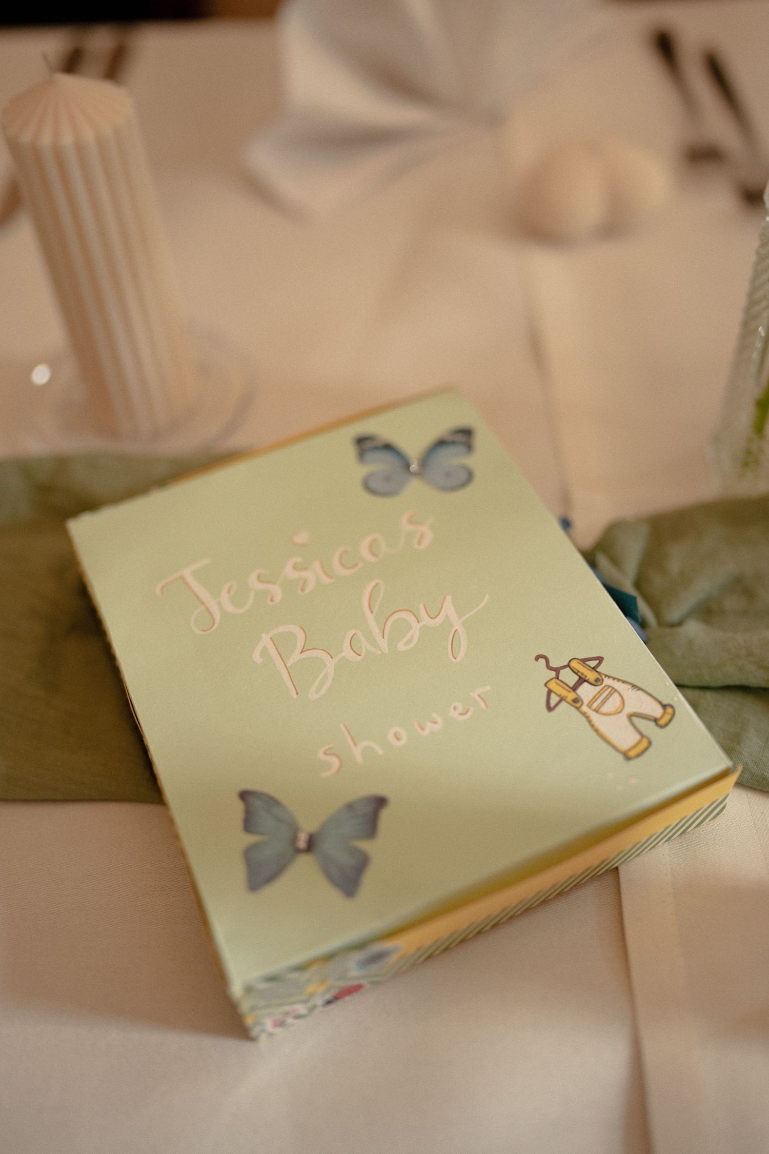 Jessica's Baby Shower green gift book with butterfly decorations on a white table setting.