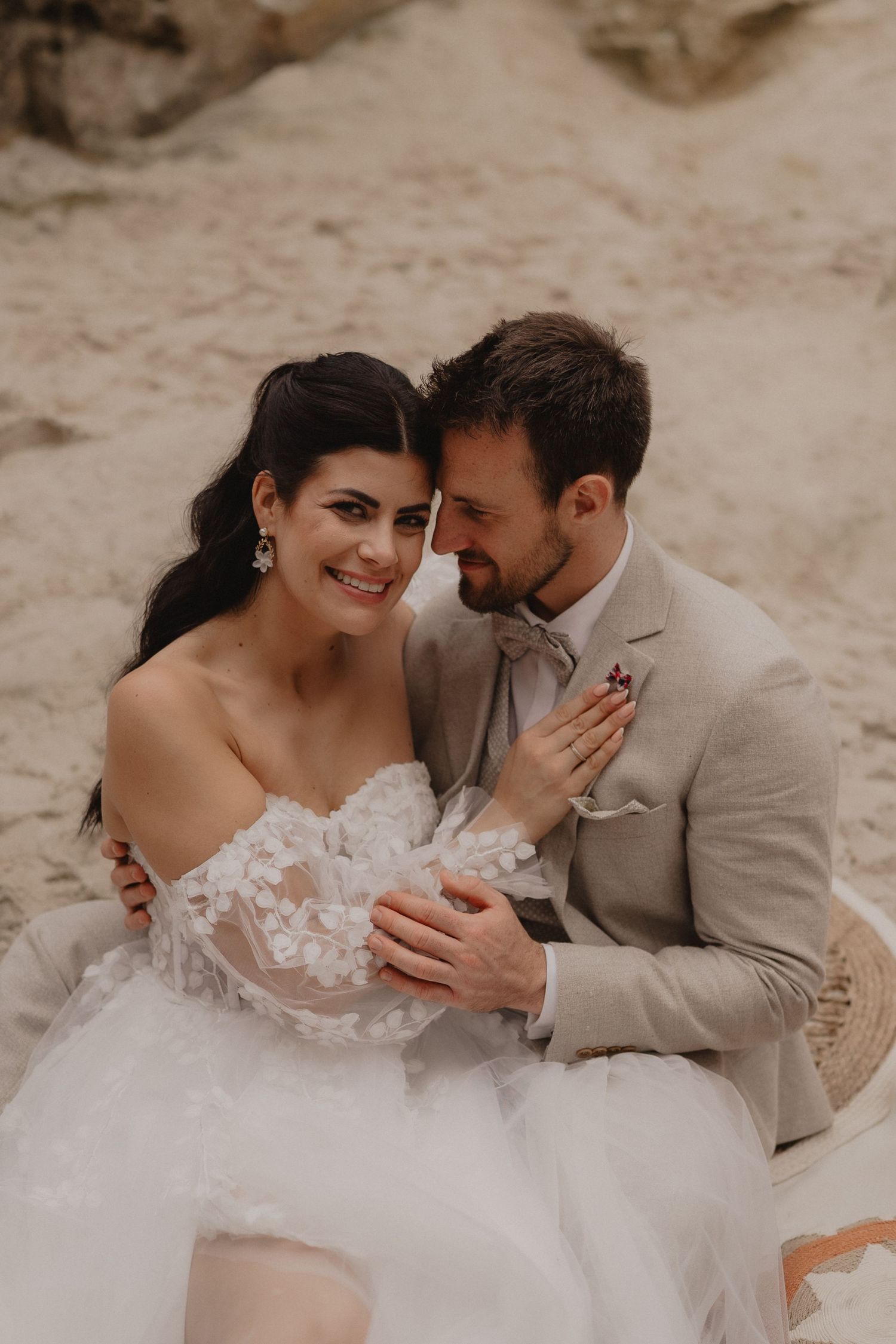 Newlyweds share tender moments on a sandy beach in neutral toned wedding attire.