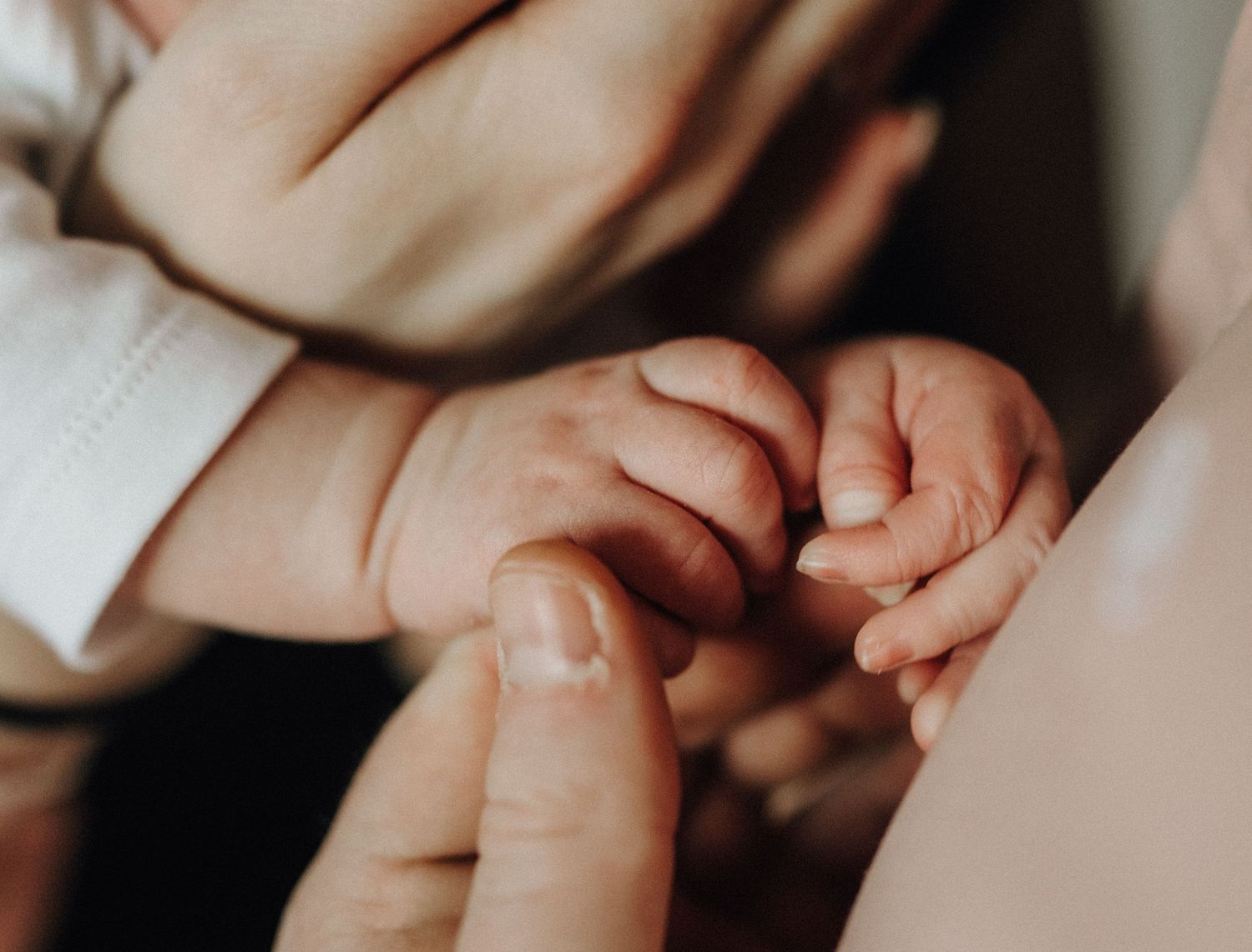 Close-up photo of newborn baby hands being gently held by adult hands in soft, warm lighting.