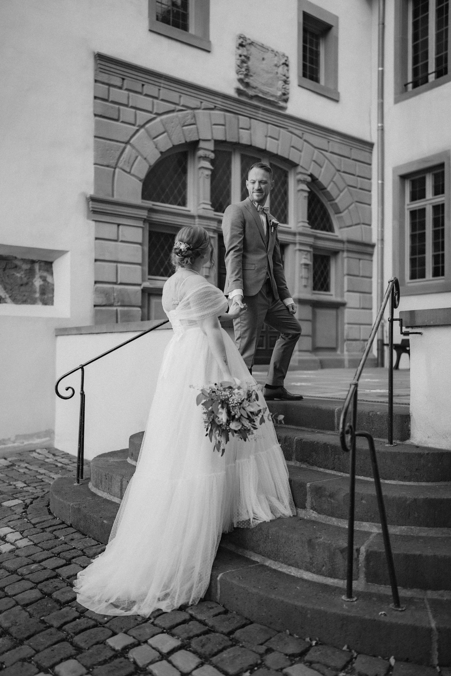 A bride in a white ballgown ascends stone steps at a historic building.