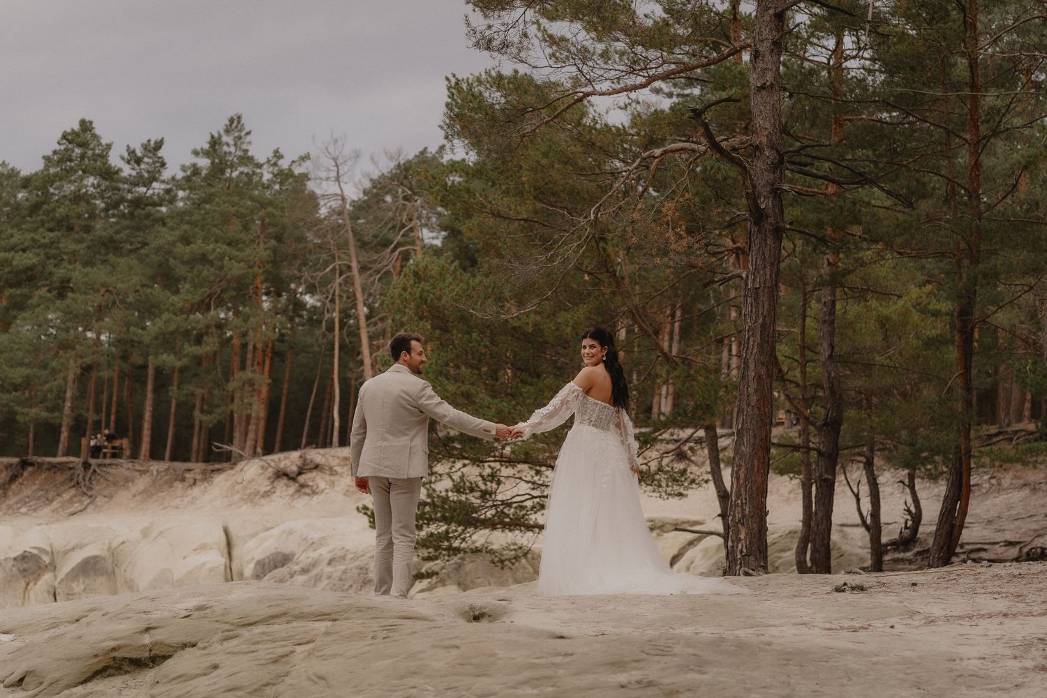 Bride and groom pose among tall pine trees in a forest setting.