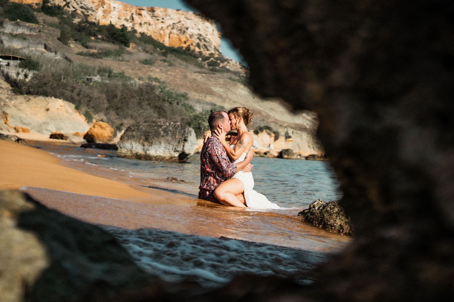 Romantic silhouettes against a dark rocky coastline during golden hour at the beach.