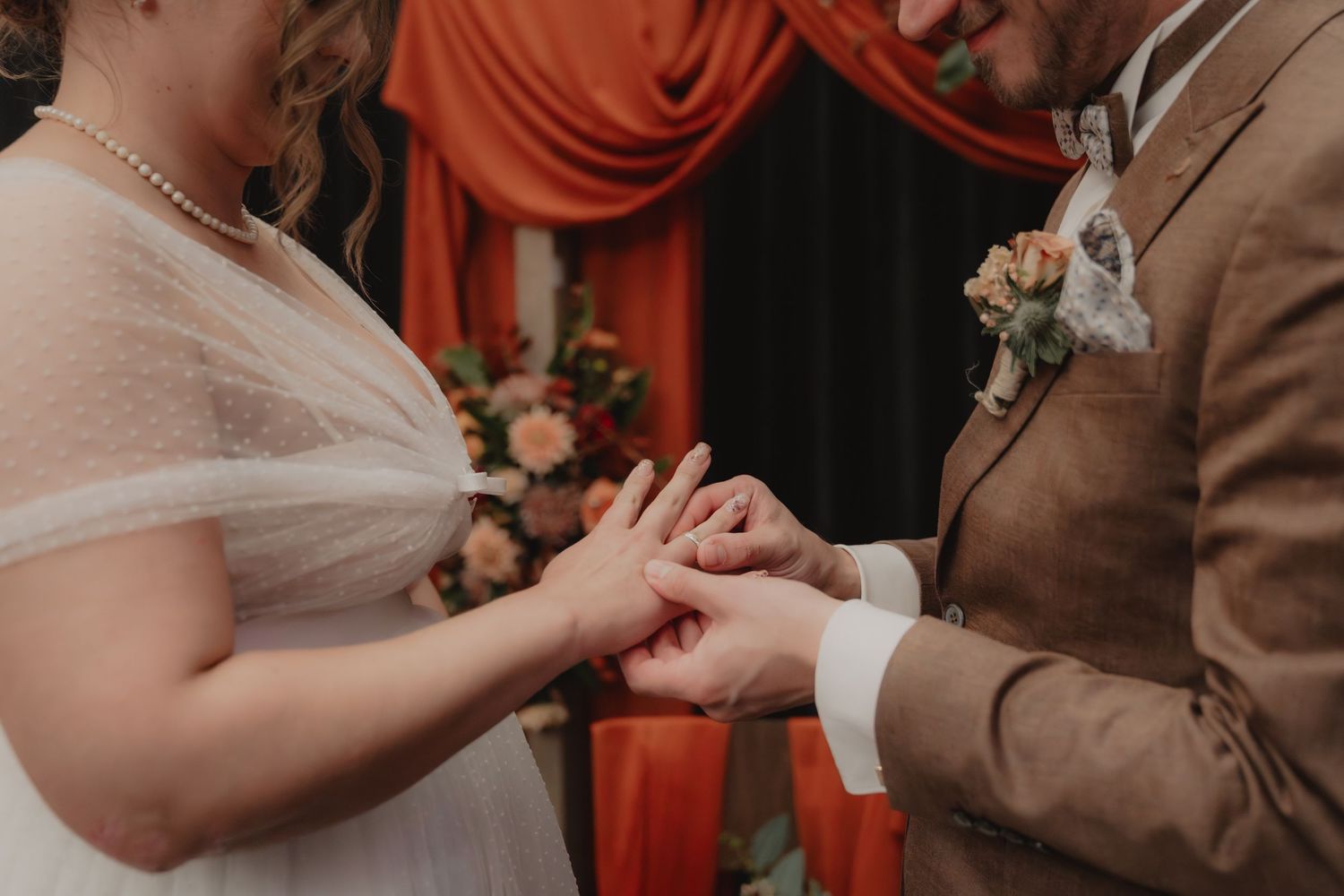 Close-up of wedding ceremony moment with orange and neutral decor details.
