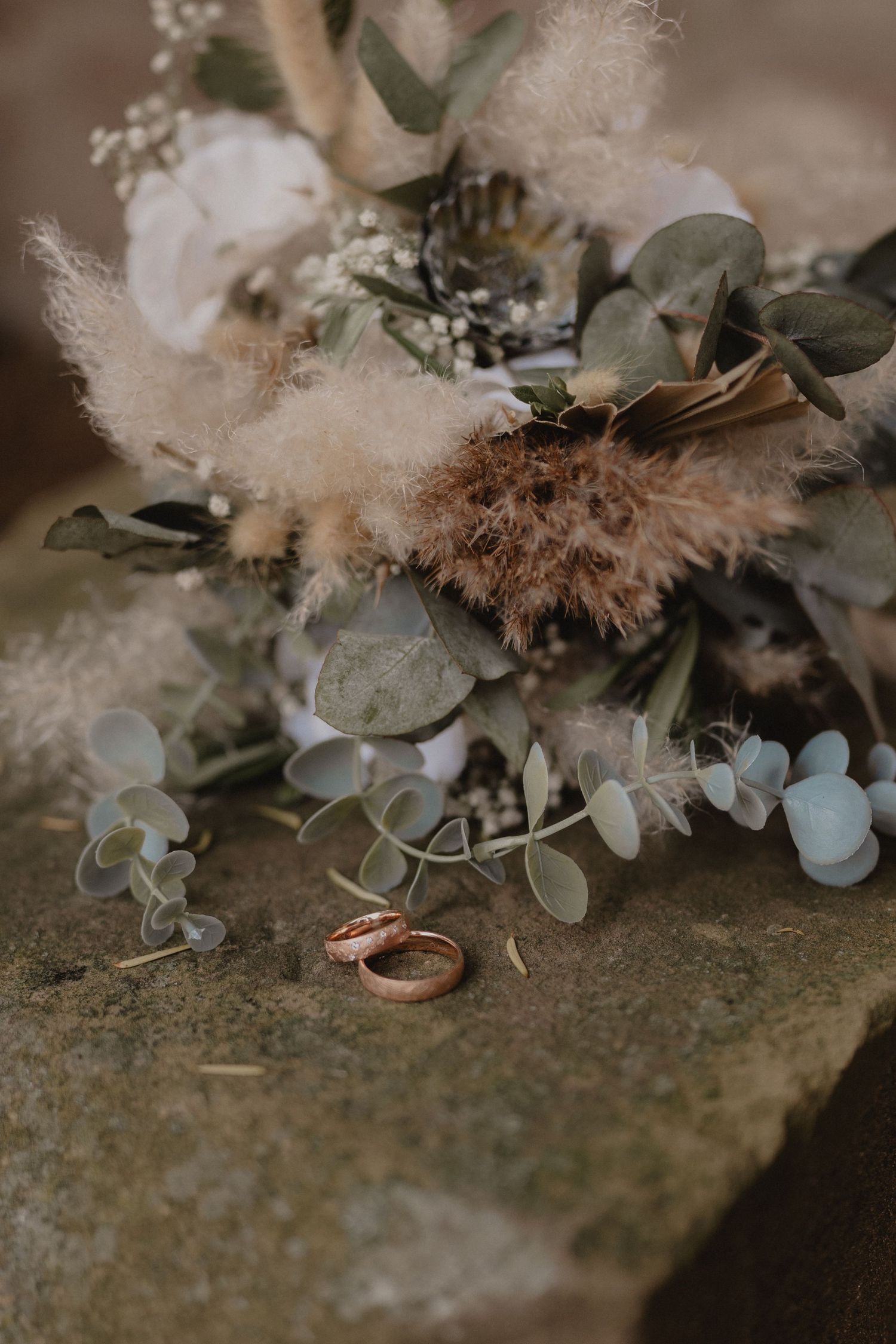 Wedding rings nestled among eucalyptus leaves and soft floral arrangements.