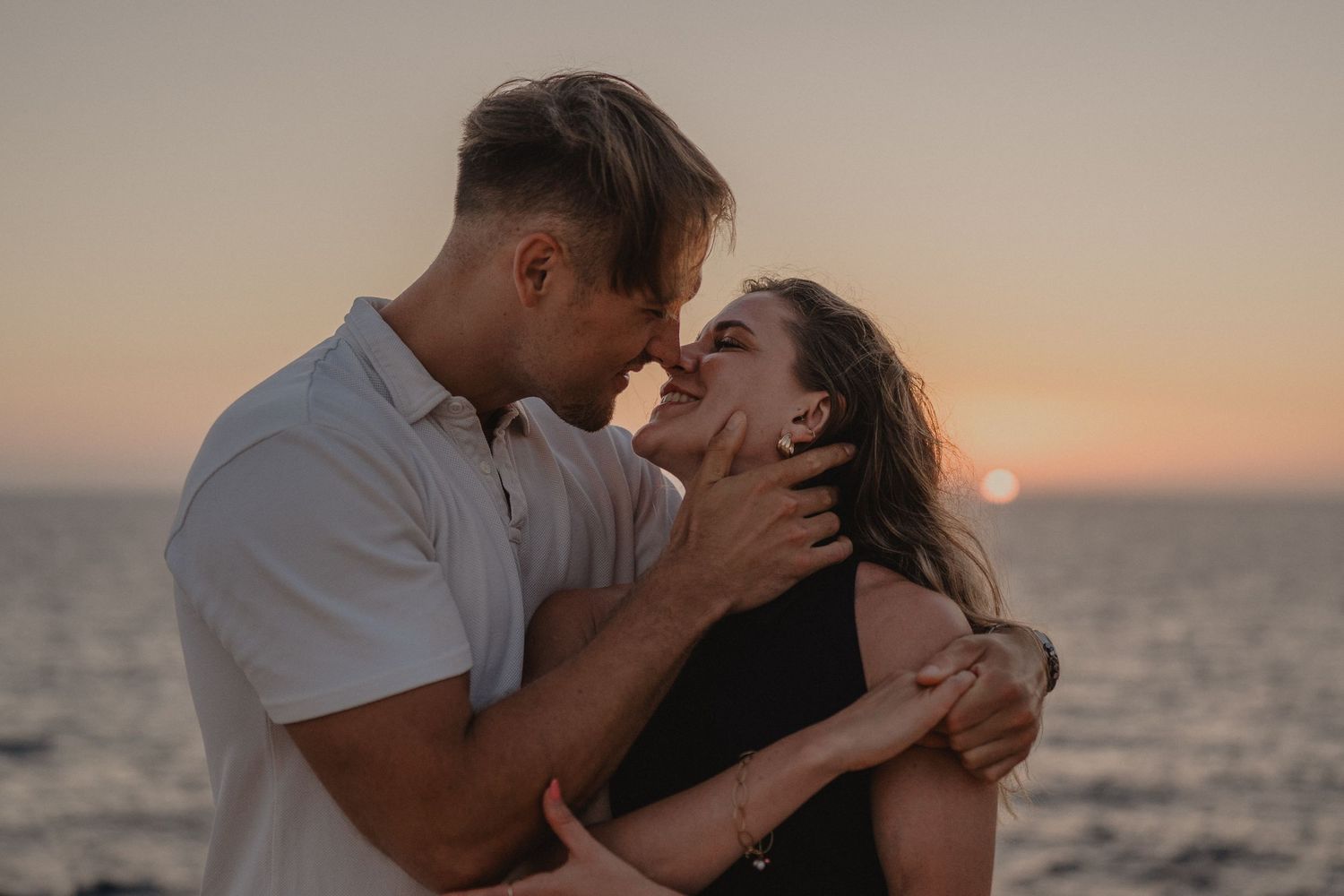 Couple sharing a romantic moment at sunset by the ocean, with warm golden hues in the background.