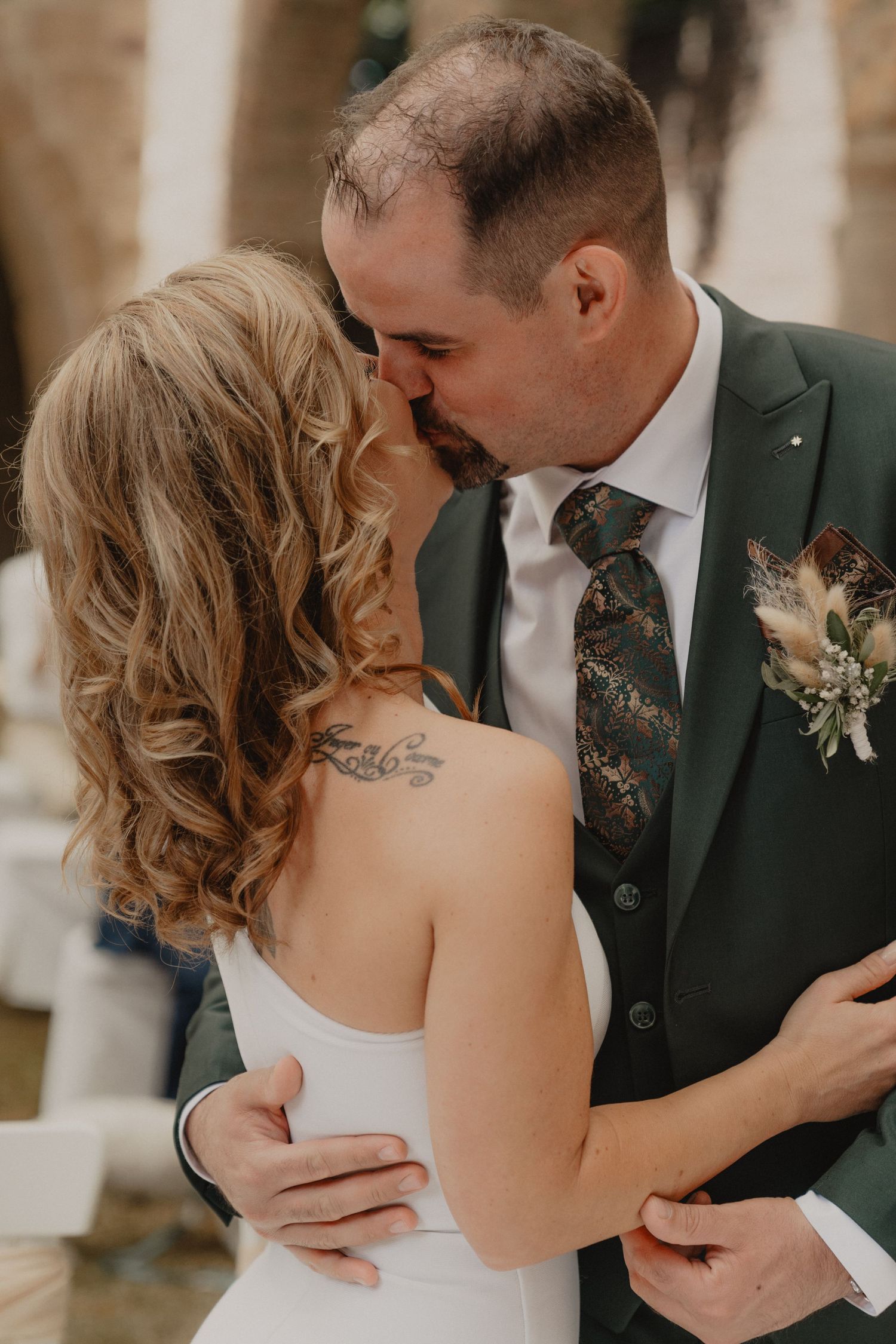 A romantic moment between newlyweds sharing a kiss at their wedding ceremony with brick archways in the background.