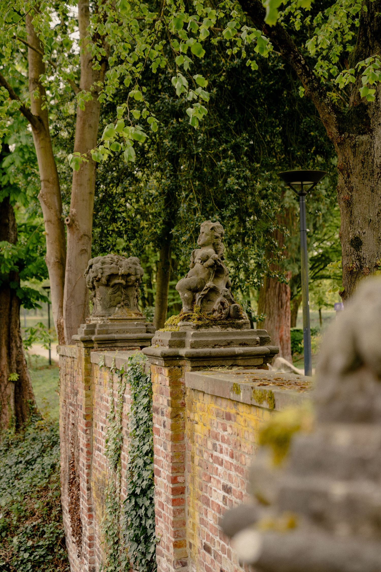 Ancient stone lion sculptures atop a weathered brick garden wall surrounded by lush green trees.