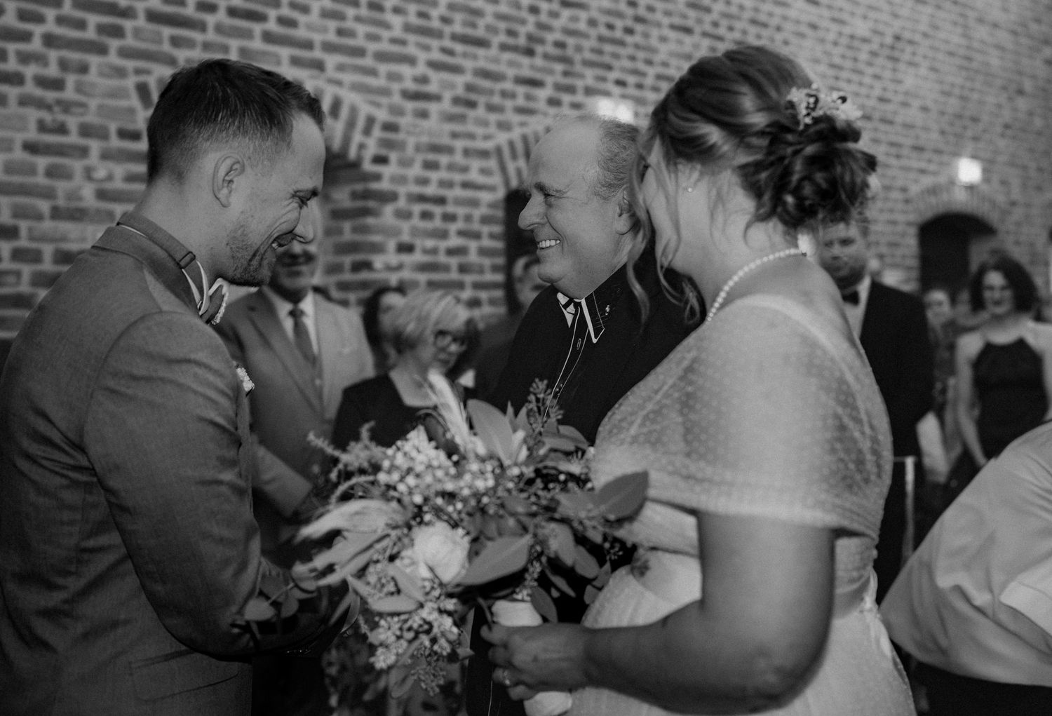 Black and white photo of wedding celebration inside rustic brick venue.
