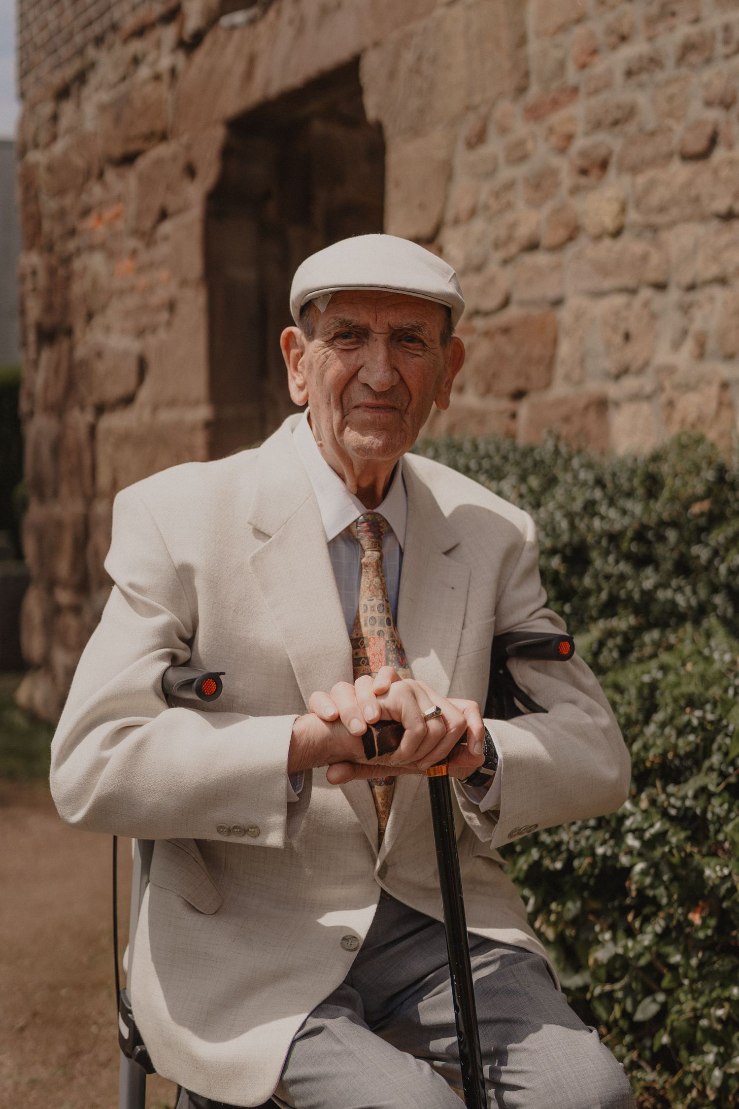 Elderly gentleman in a light colored suit sitting outdoors with a walking cane.