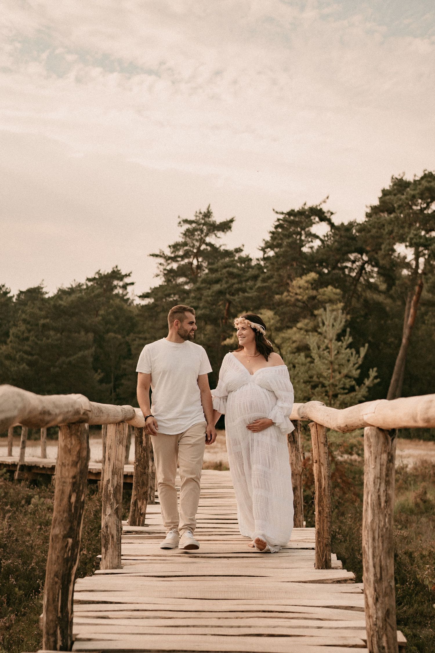 Couple walking hand in hand on a rustic wooden boardwalk surrounded by pine trees.