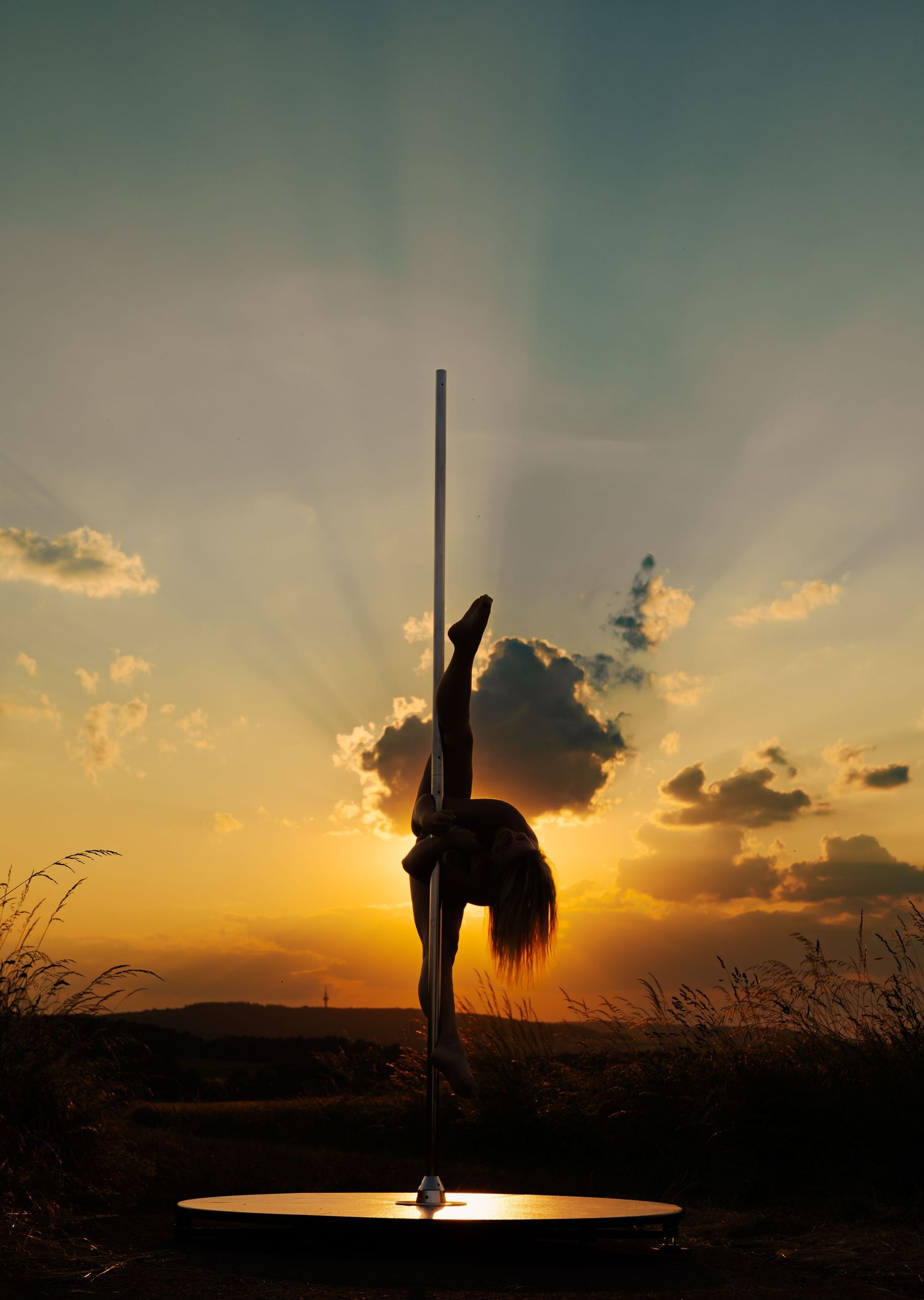 Silhouette of a pole dancer performing against a stunning golden sunset sky with dramatic clouds.