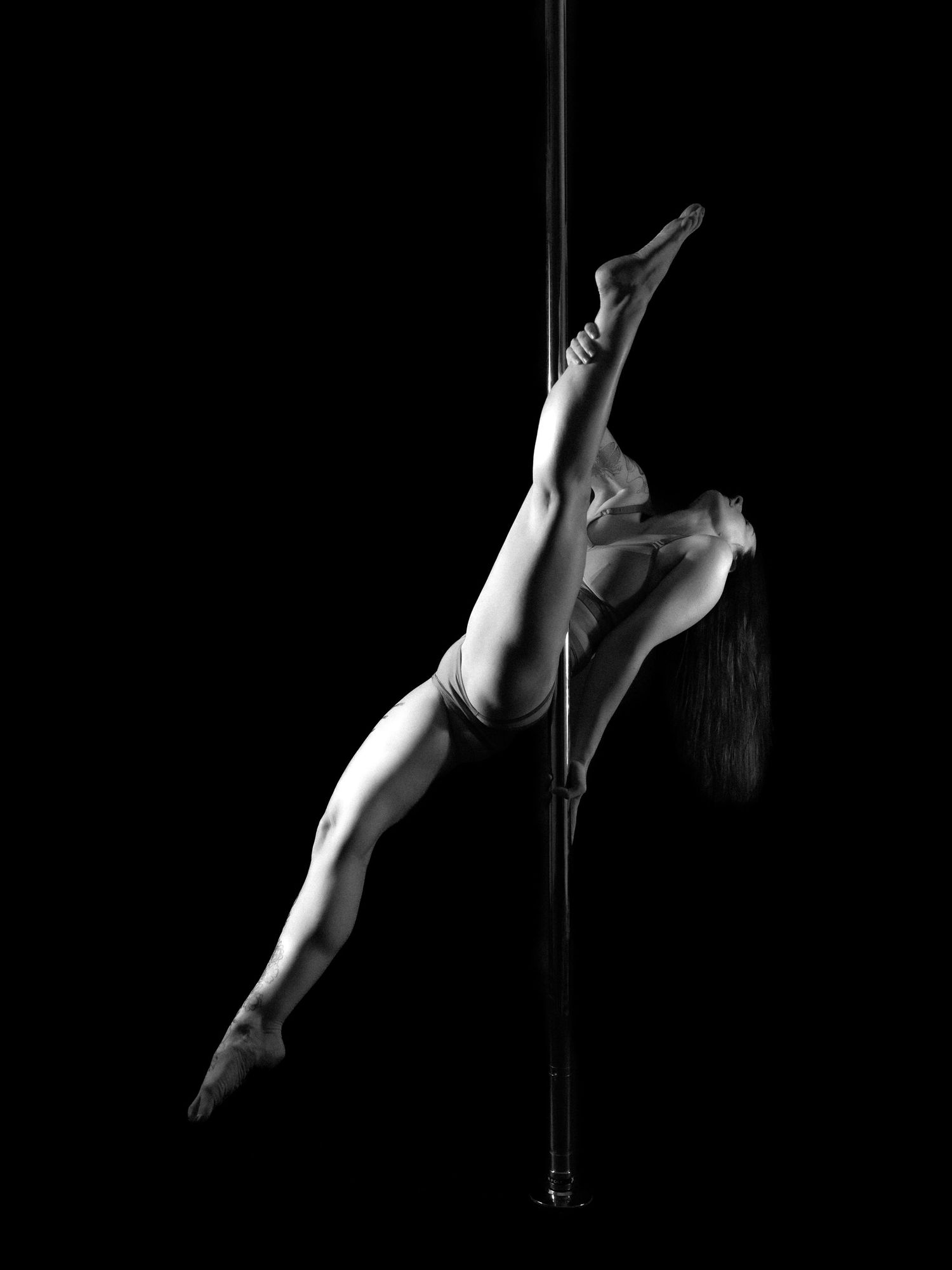 Black and white photo of a pole dancer performing an impressive horizontal hold on a vertical pole.