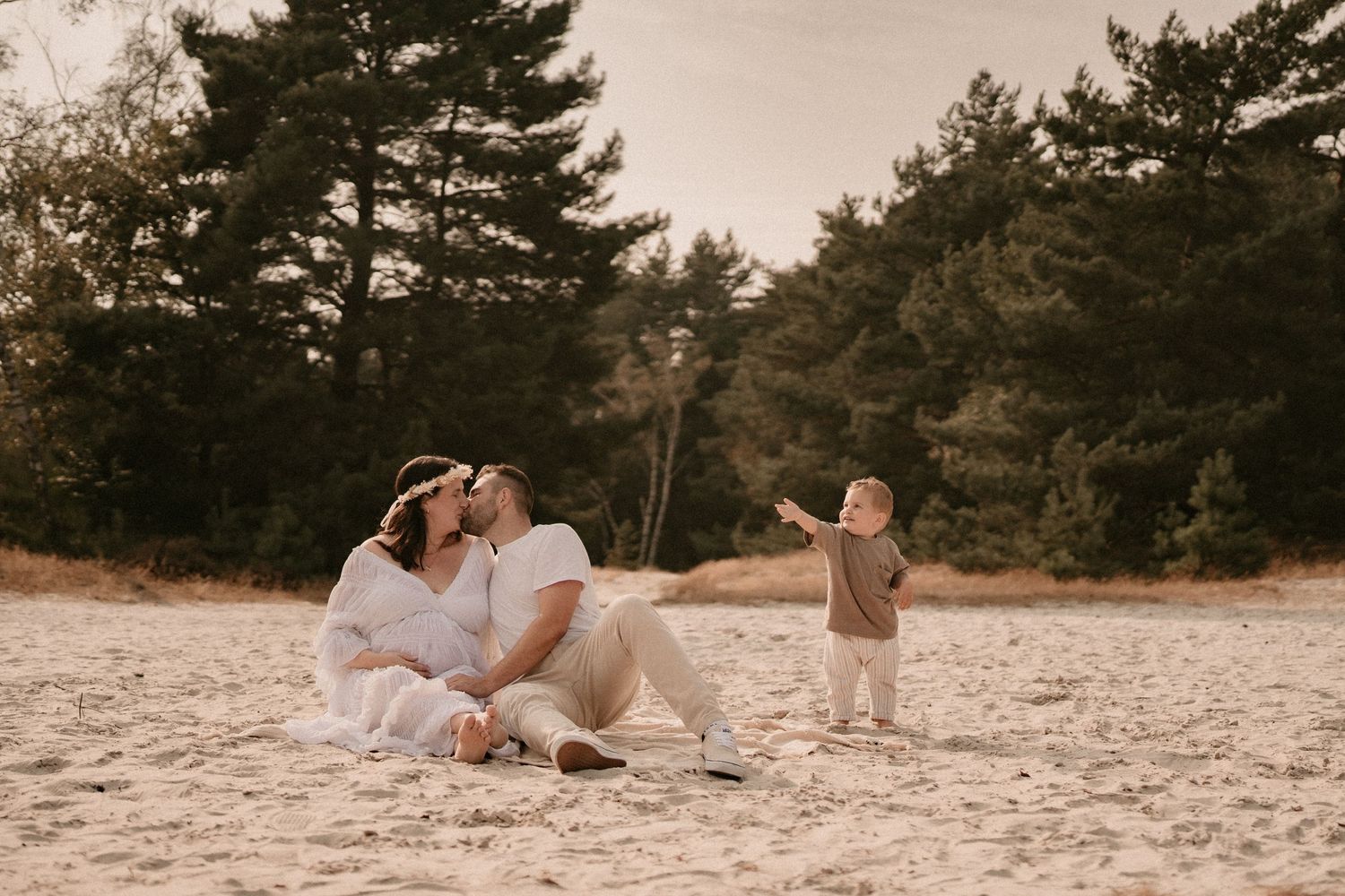 Romantic couple's photoshoot on sandy beach with pine trees in background.