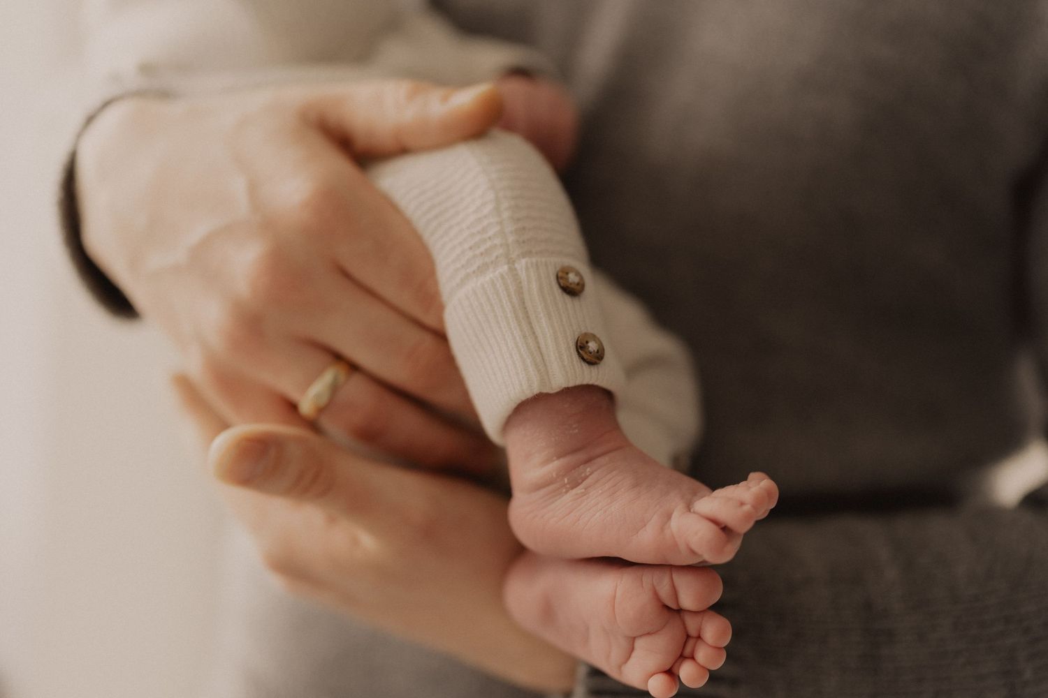 Close-up of tiny baby feet and hands against neutral background.