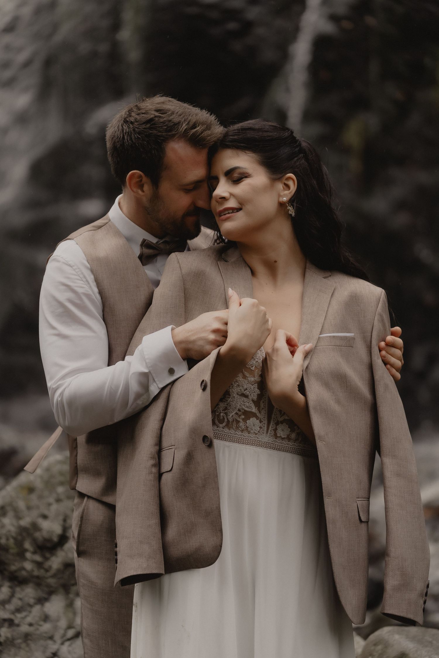 Romantic wedding portrait against a waterfall backdrop with neutral toned attire.