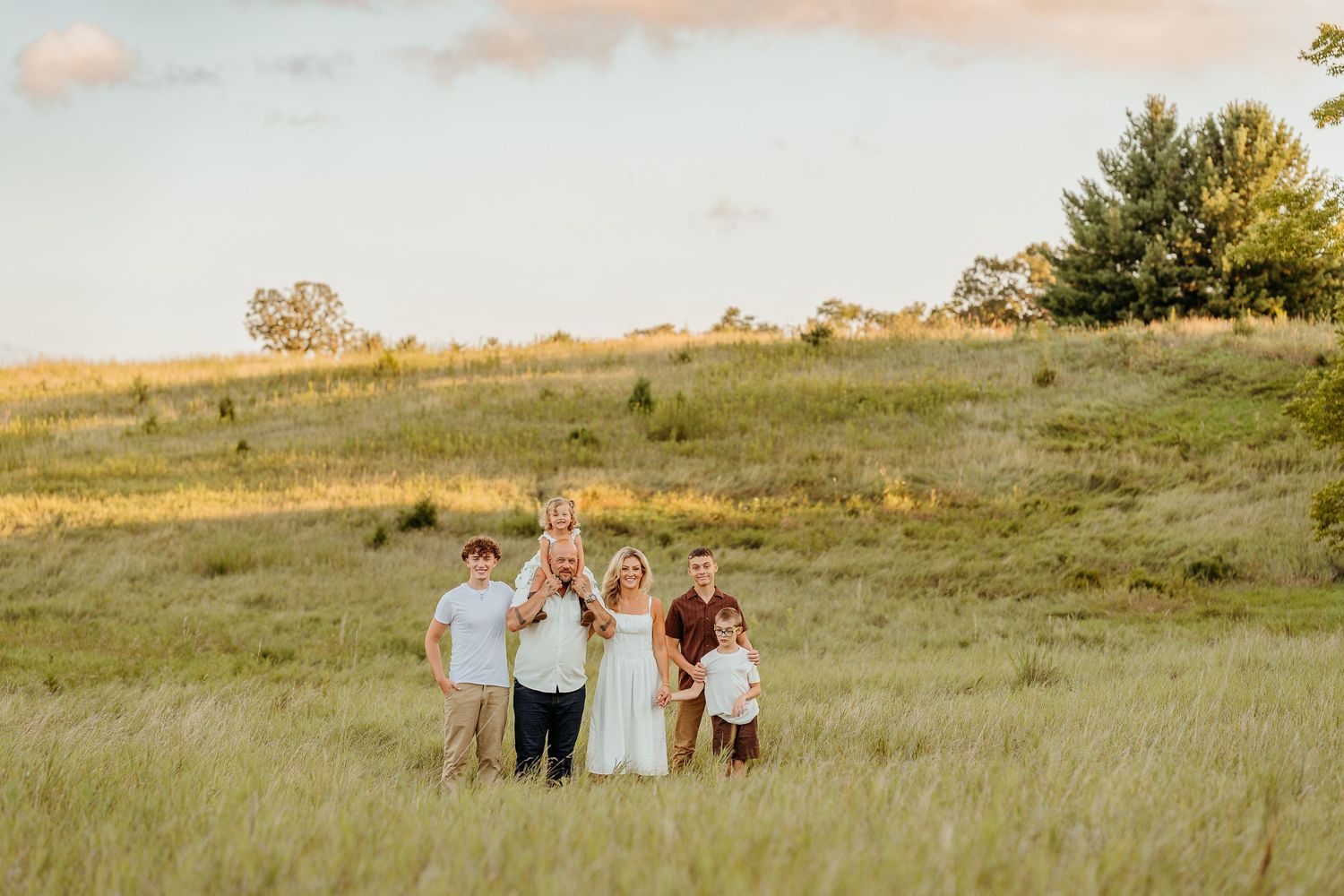 A family stands sits together on a blanket in a golden field during sunset for a casual outdoor photoshoot in the lake country WI