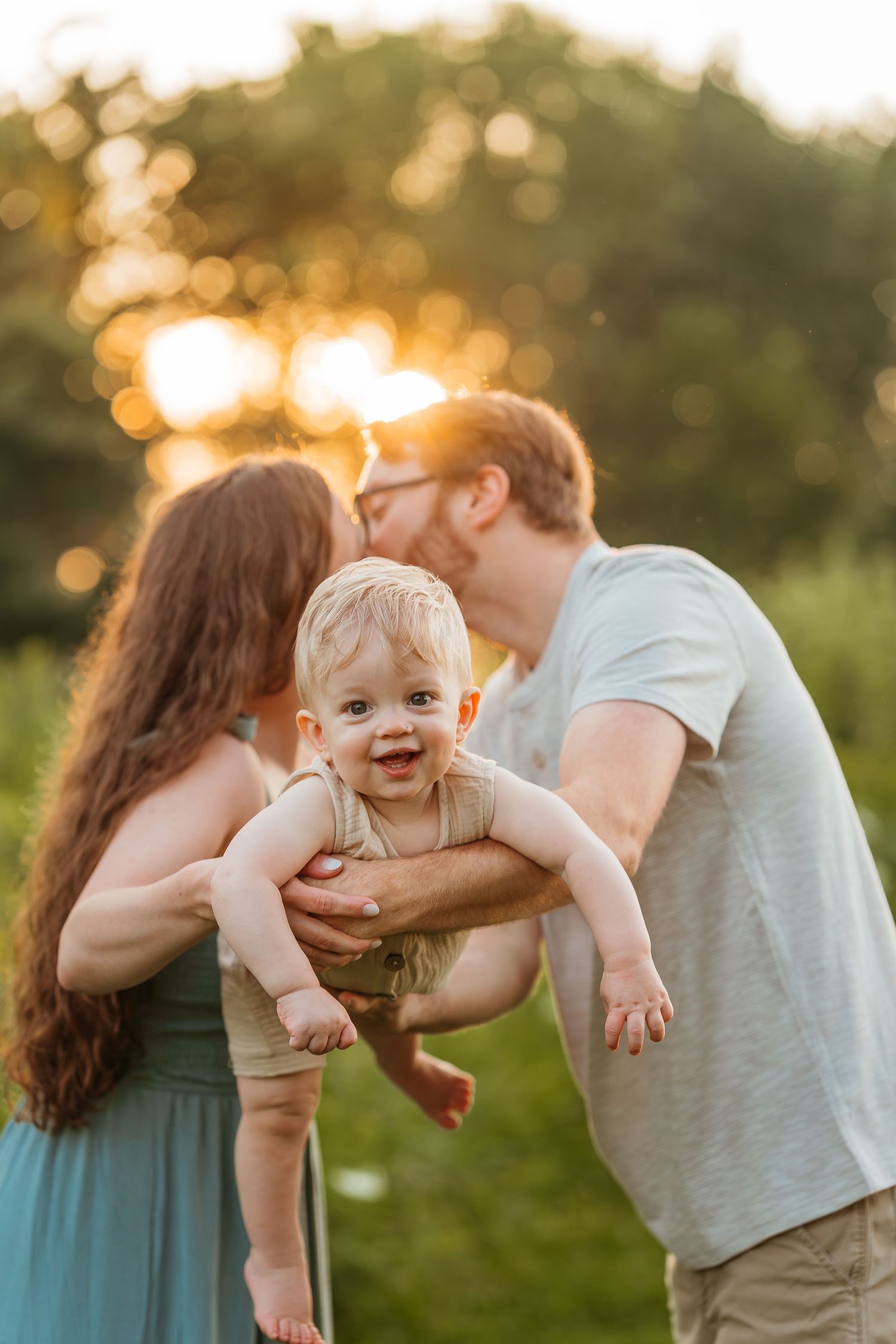 Happy baby smiling while being held by parents during golden hour outdoor milestone photoshoot.