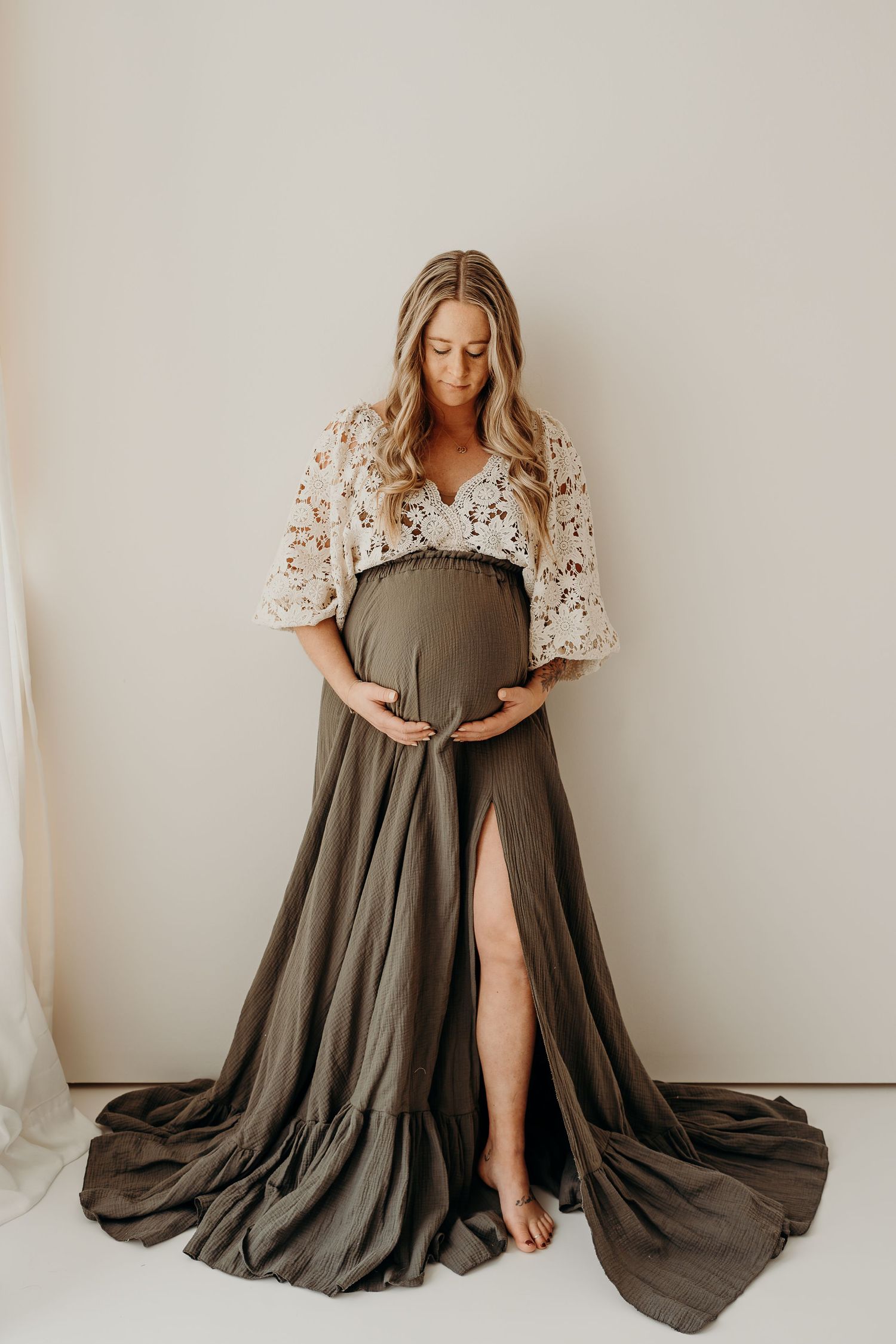 Maternity portrait in an olive dress with floral sleeves against white backdrop.