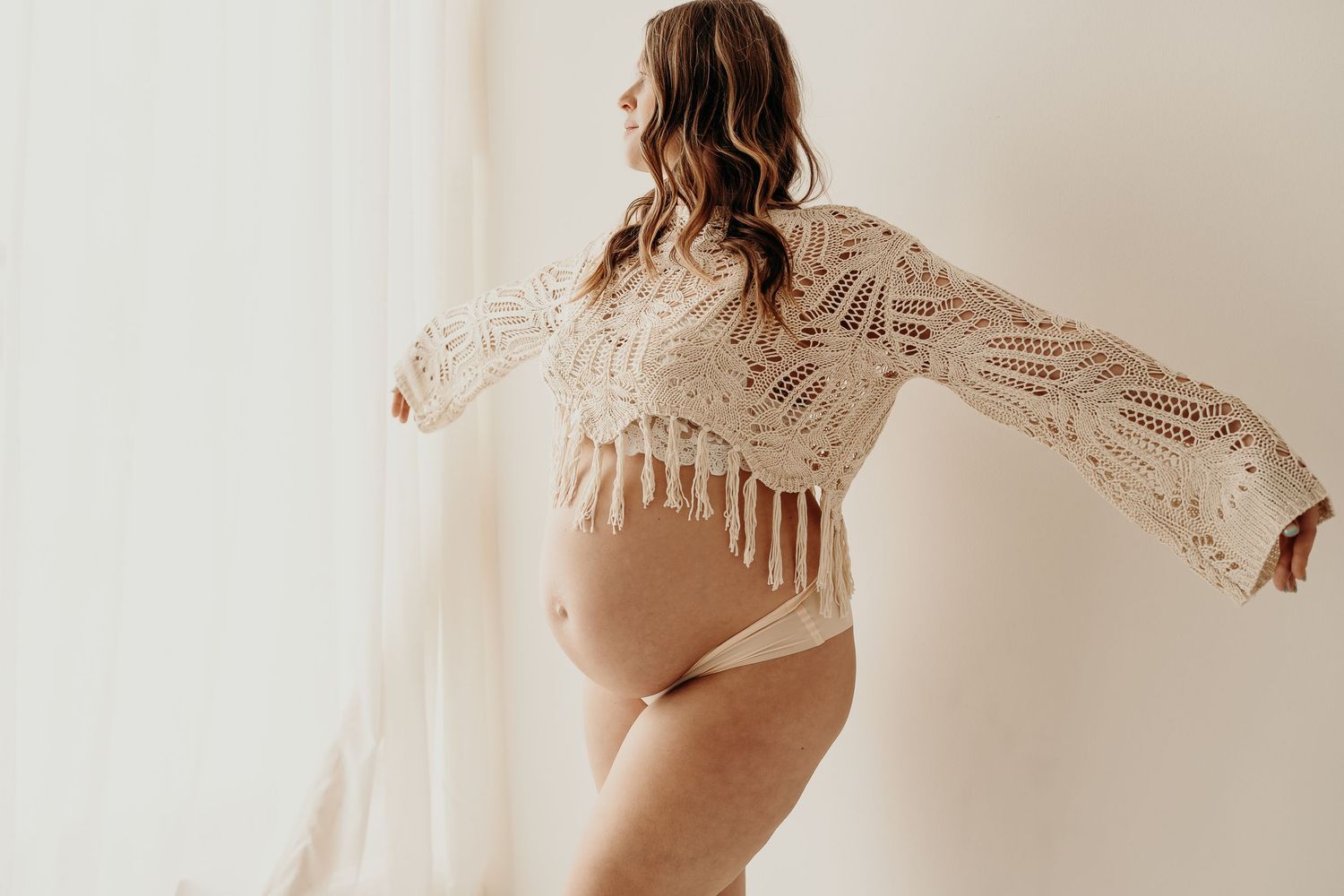 Pregnant mom in neutral dress standing by a bright window at SlateStudio in East Troy, Wisconsin.