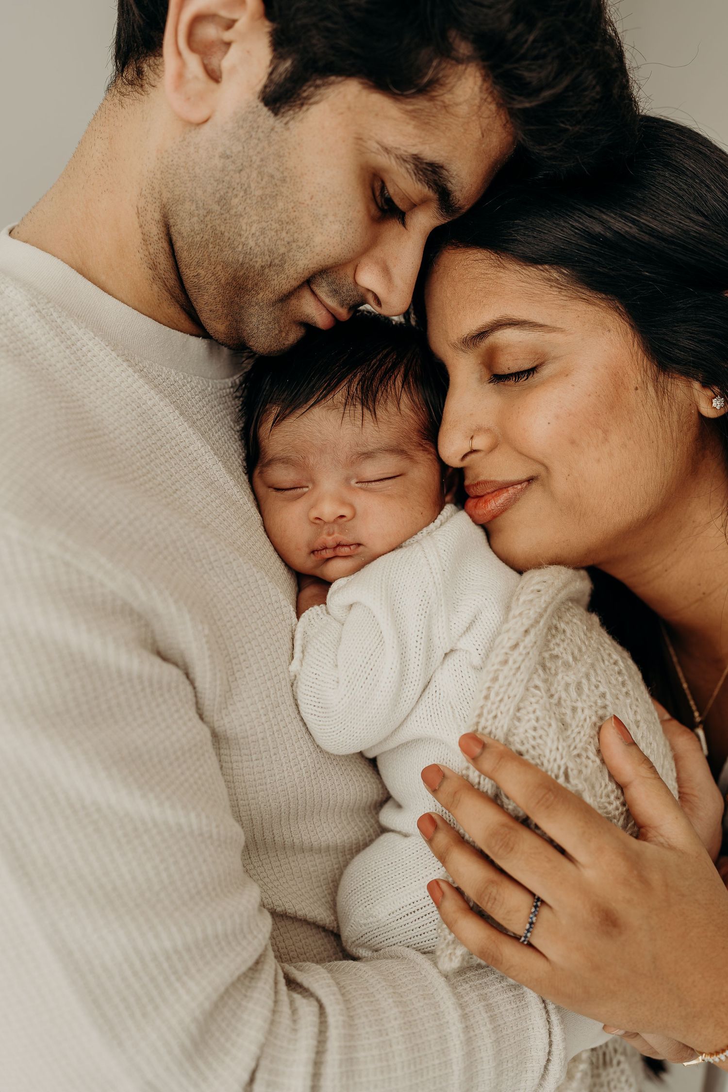 Parents tenderly holding their sleeping newborn baby, sharing an intimate family moment in soft neutral tones. Newborn photography tips