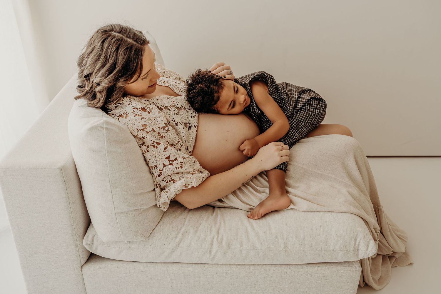 Maternity photographer in East Troy, Wisconsin photographing parents and their little one snuggled together on the studio bed.