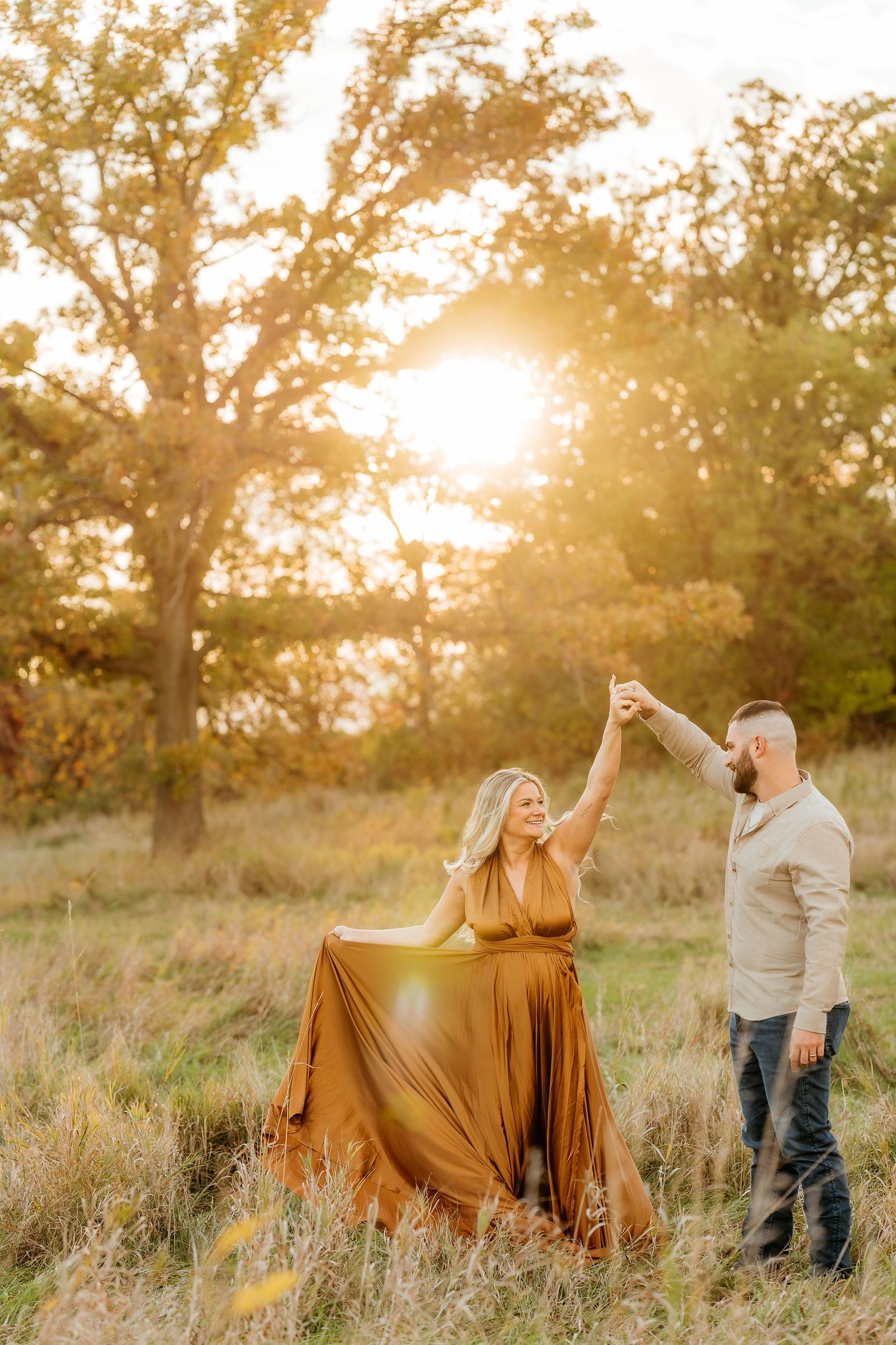 Couple dancing in a sunlit field during golden hour with flowing mustard dress showcasing a baby bump/maternity session.