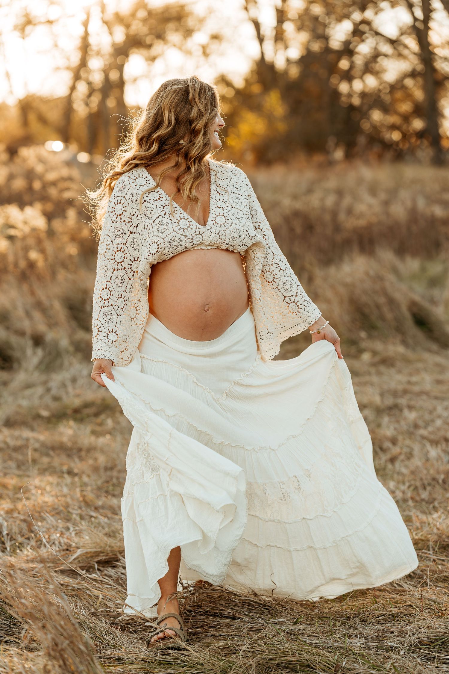 White lace maternity dress photographed outdoors during golden hour in rustic field setting.