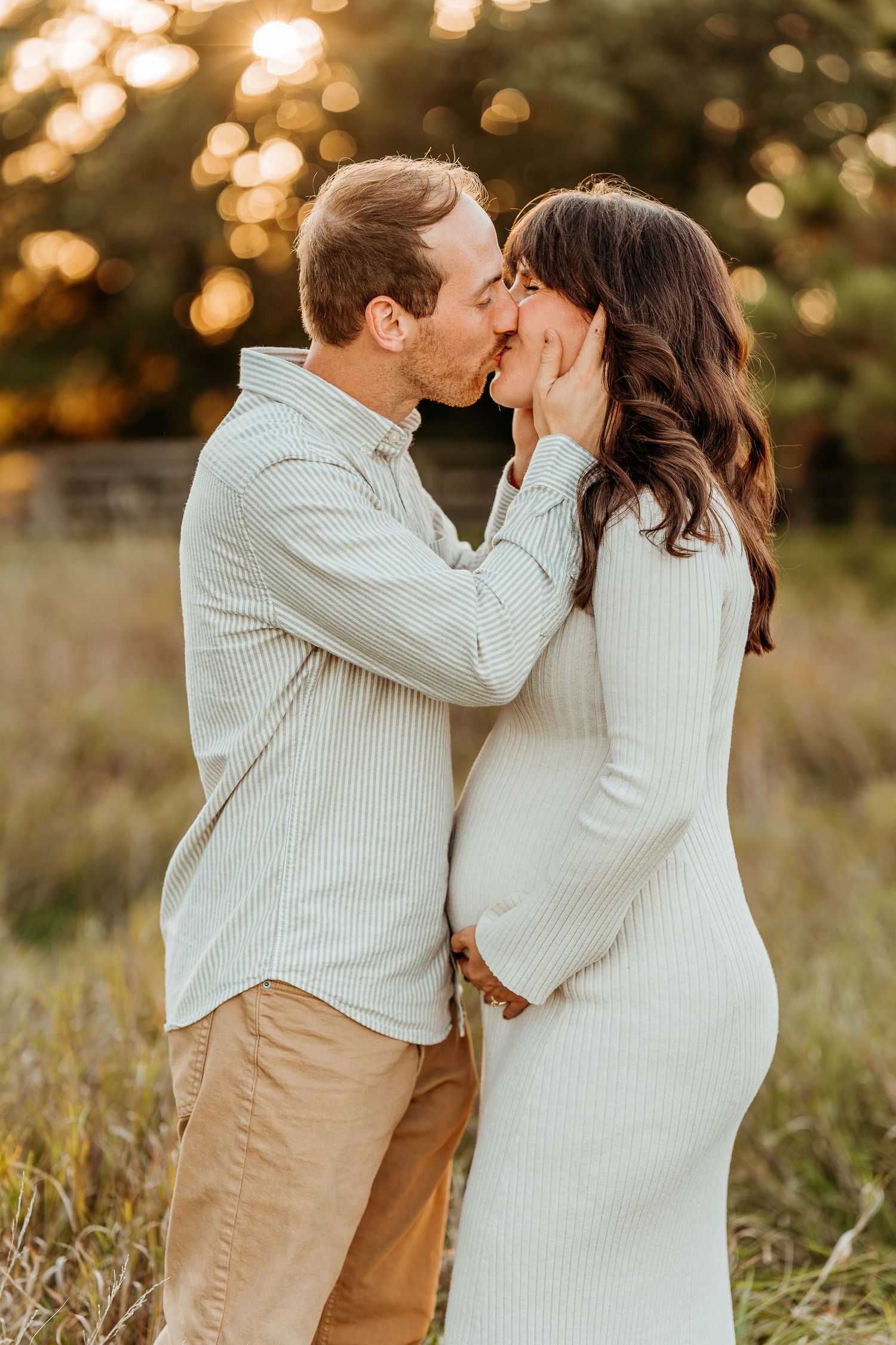 Romantic maternity photos of couple embracing in field during golden hour sunset.