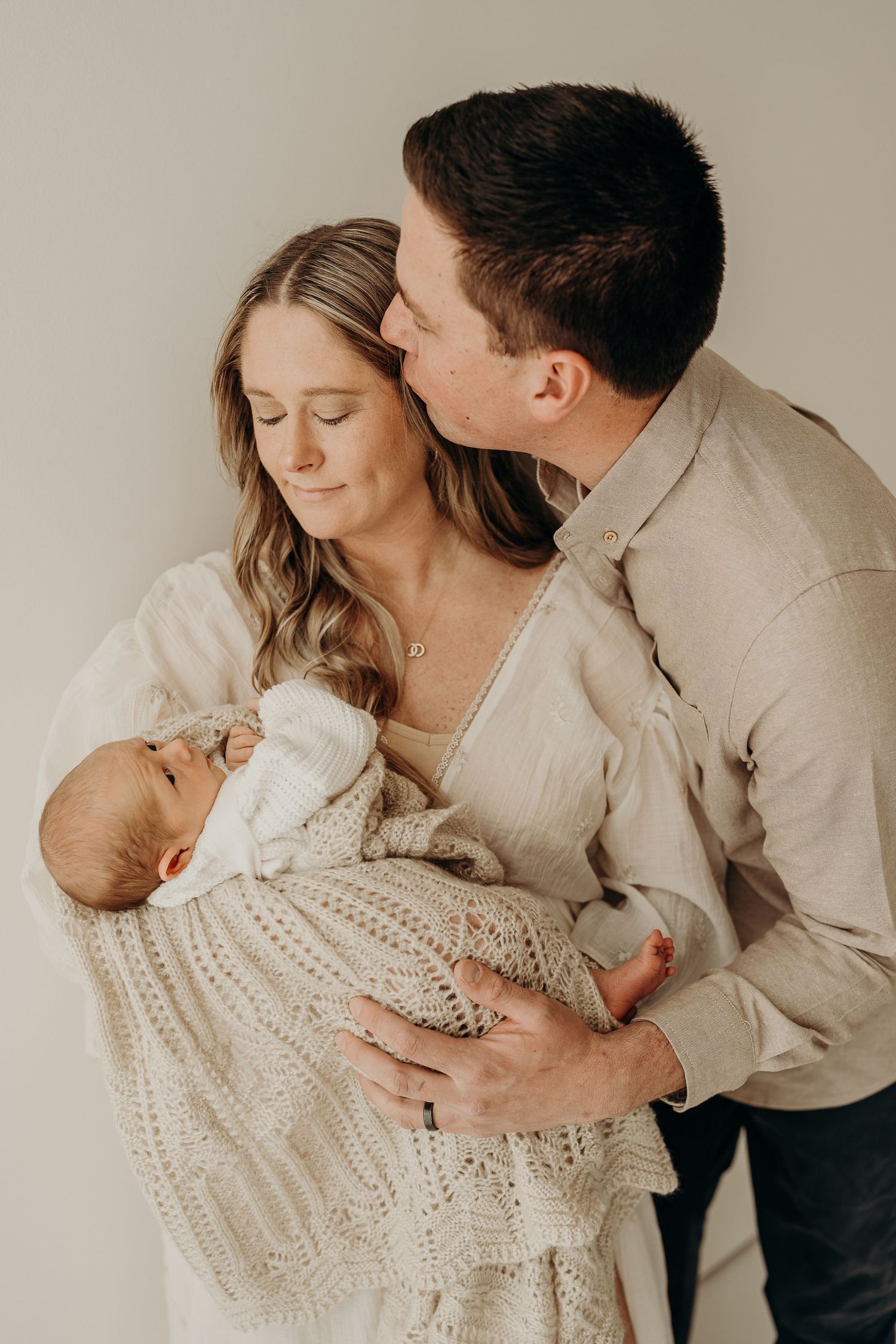 A series of intimate family portraits in neutral tones showing tender moments between parents and their newborn baby.