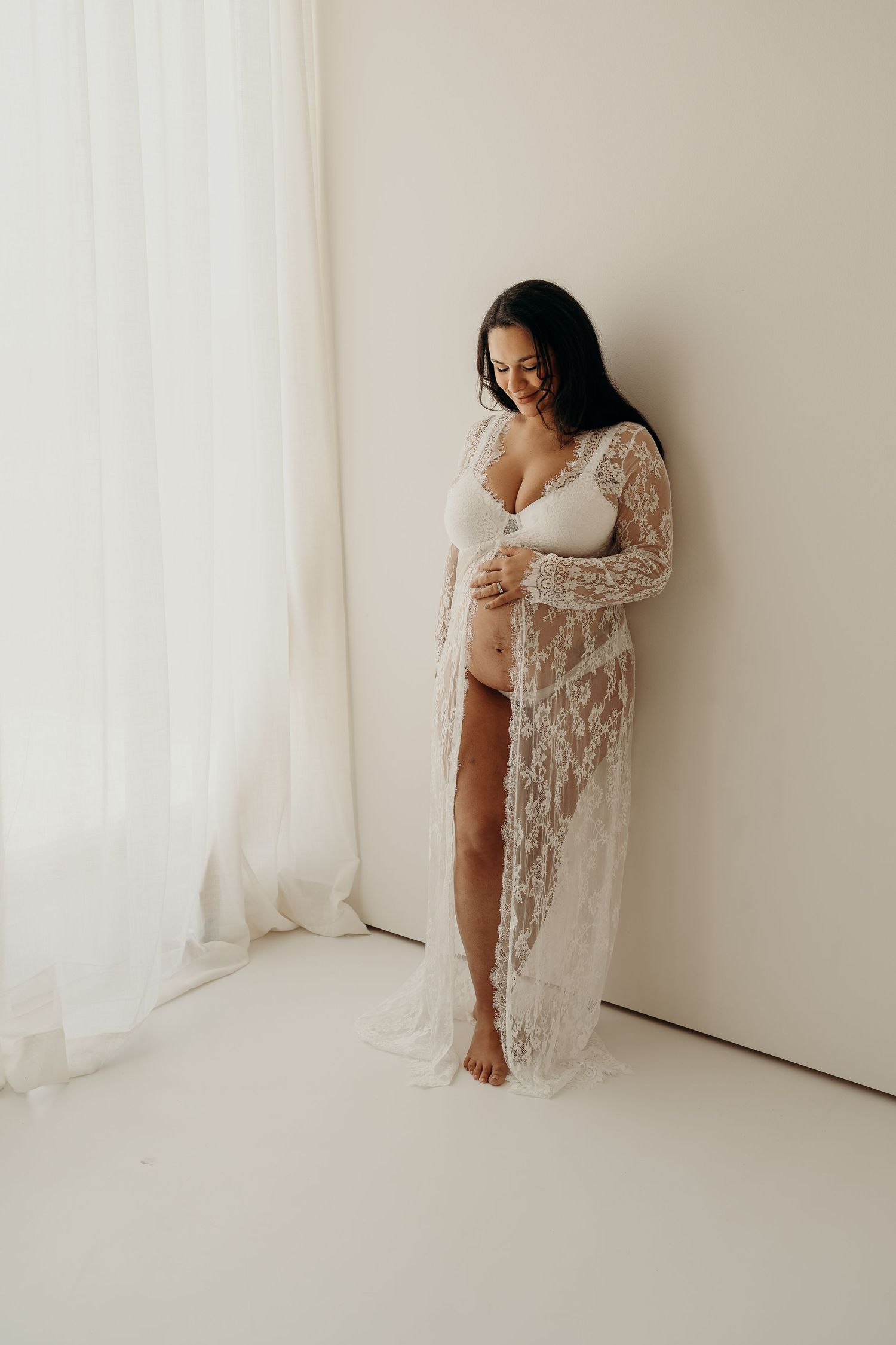 Delicate white lace maternity boudoir photos against minimalist white studio backdrop.