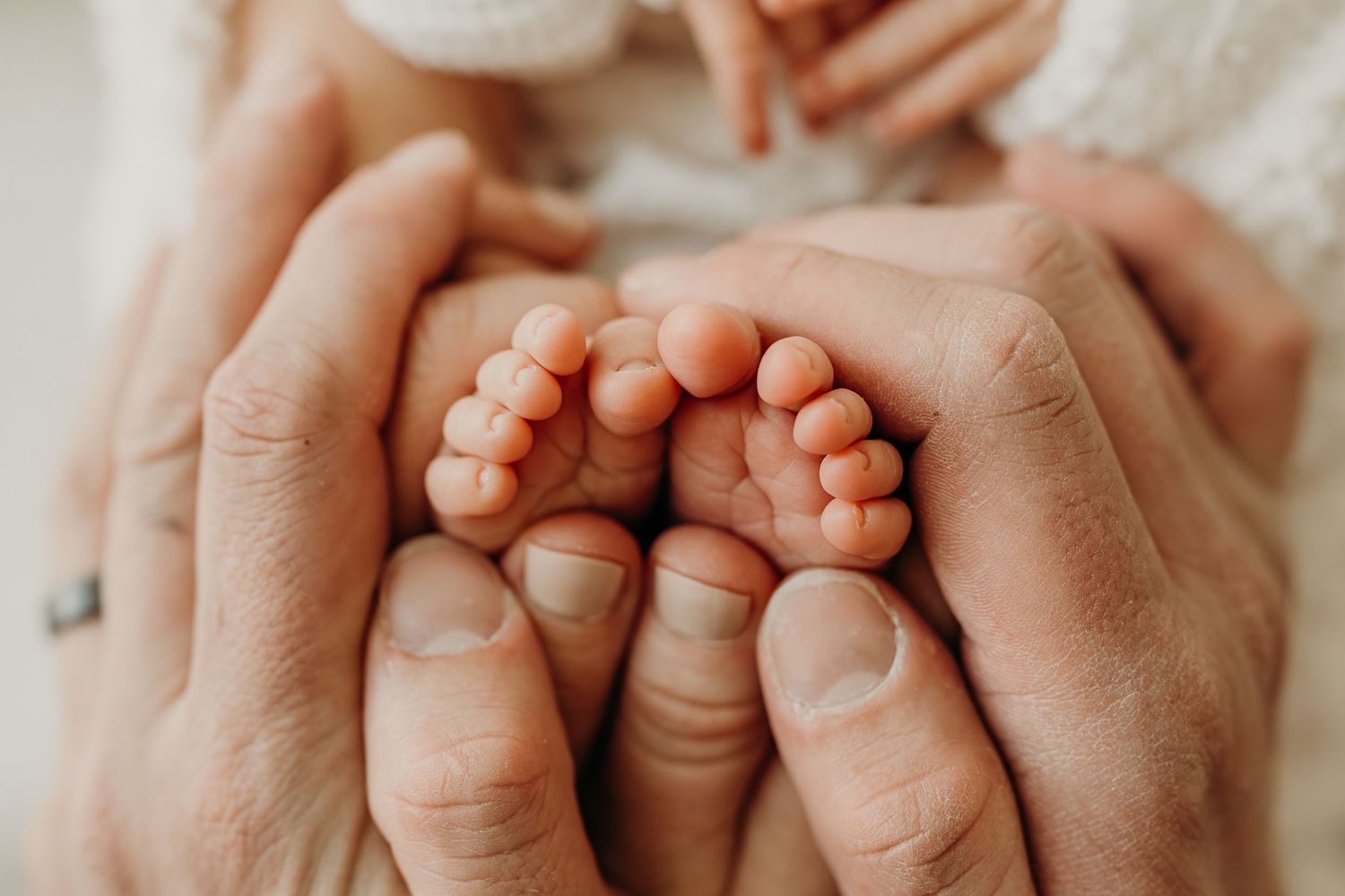 Adult hands gently cradling tiny newborn baby feet, symbolizing love and new parenthood. Perfect pose for a newborn session