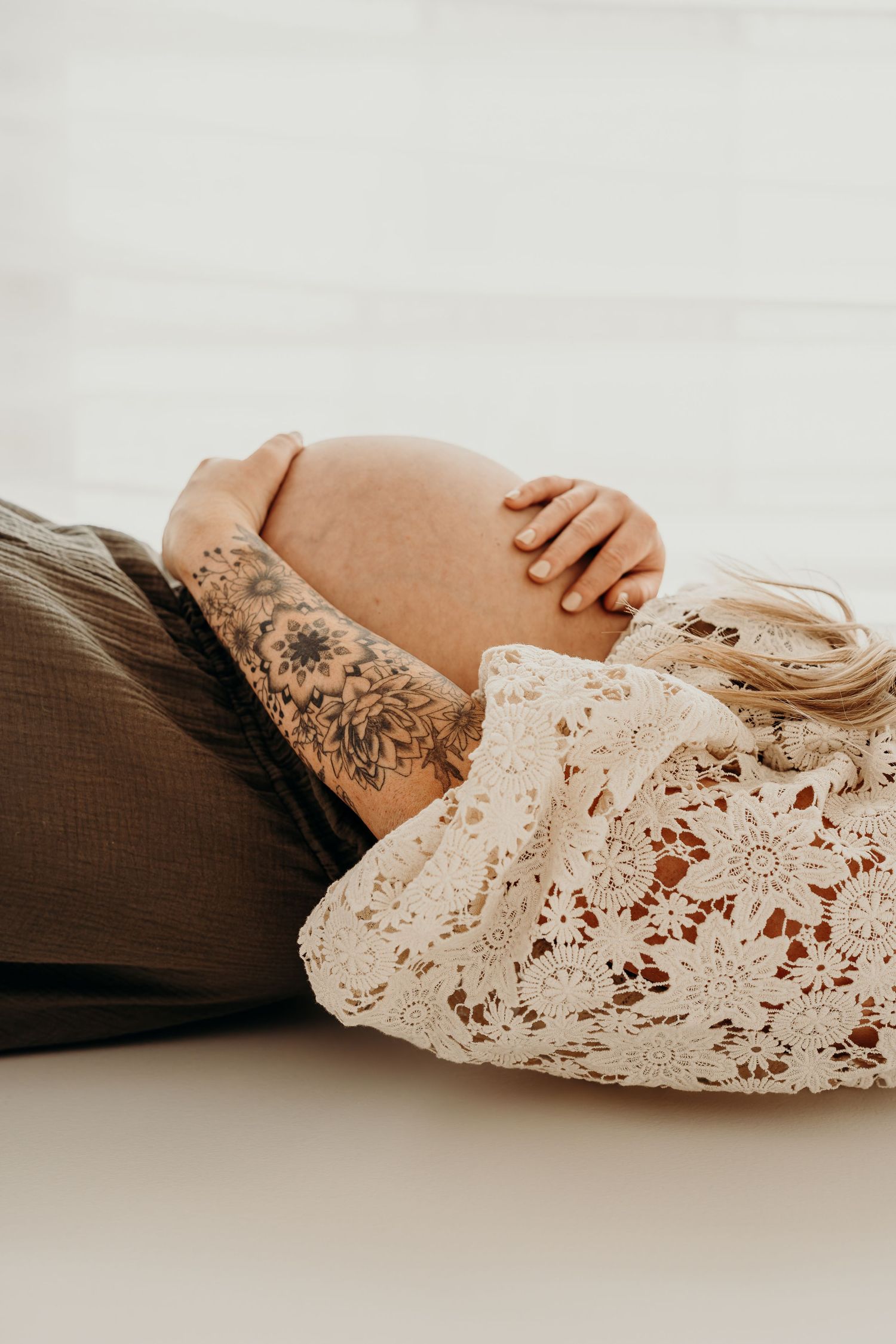 Expecting mom laying on a cozy studio bed with her hands resting gently on her bump.