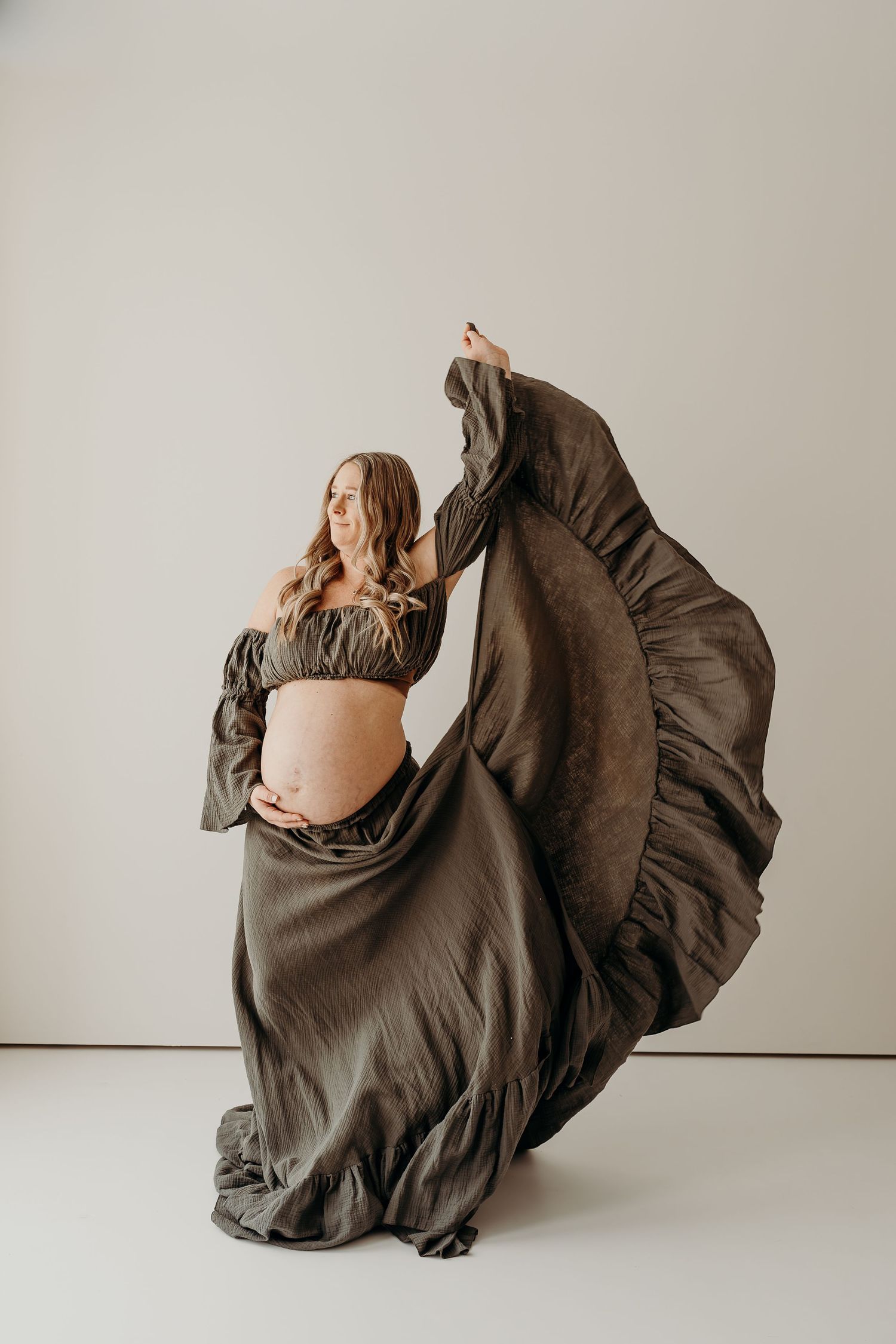 Pregnant mom swinging her dress, standing by a bright window at SlateStudio in East Troy, Wisconsin.