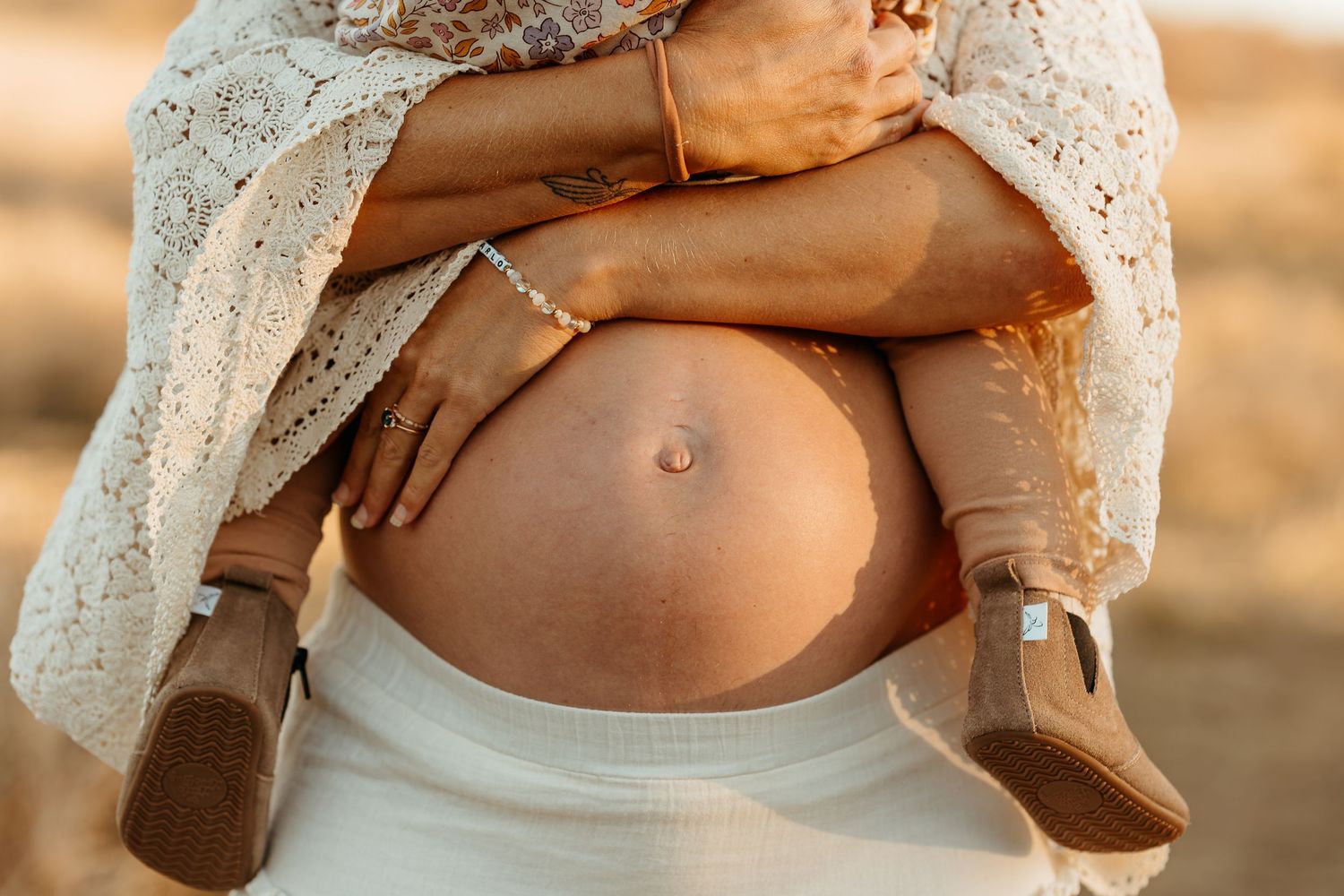 Close-up maternity photos showing bare pregnant belly with delicate lace details.