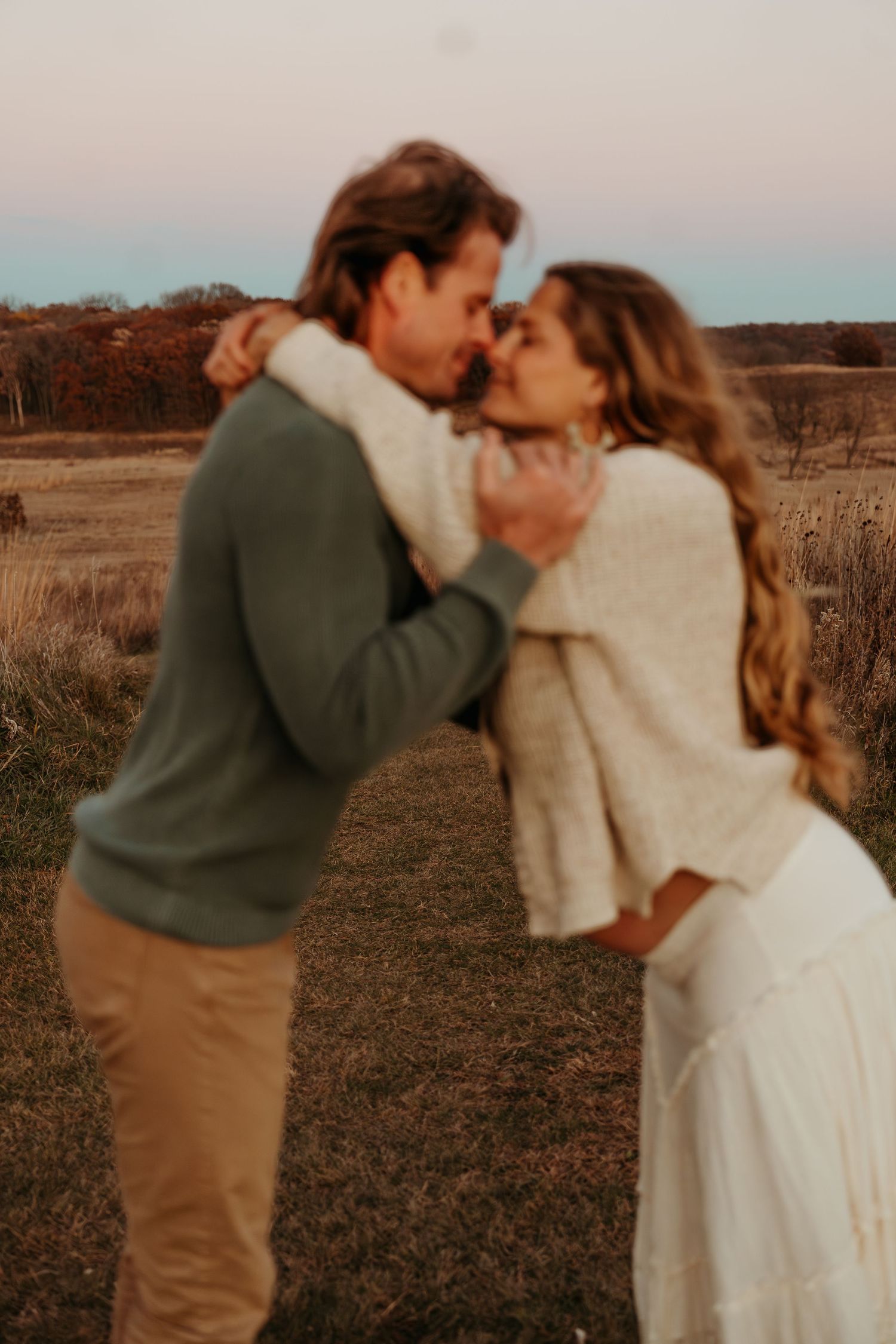 Romantic couple dancing together in a rustic field during golden hour.