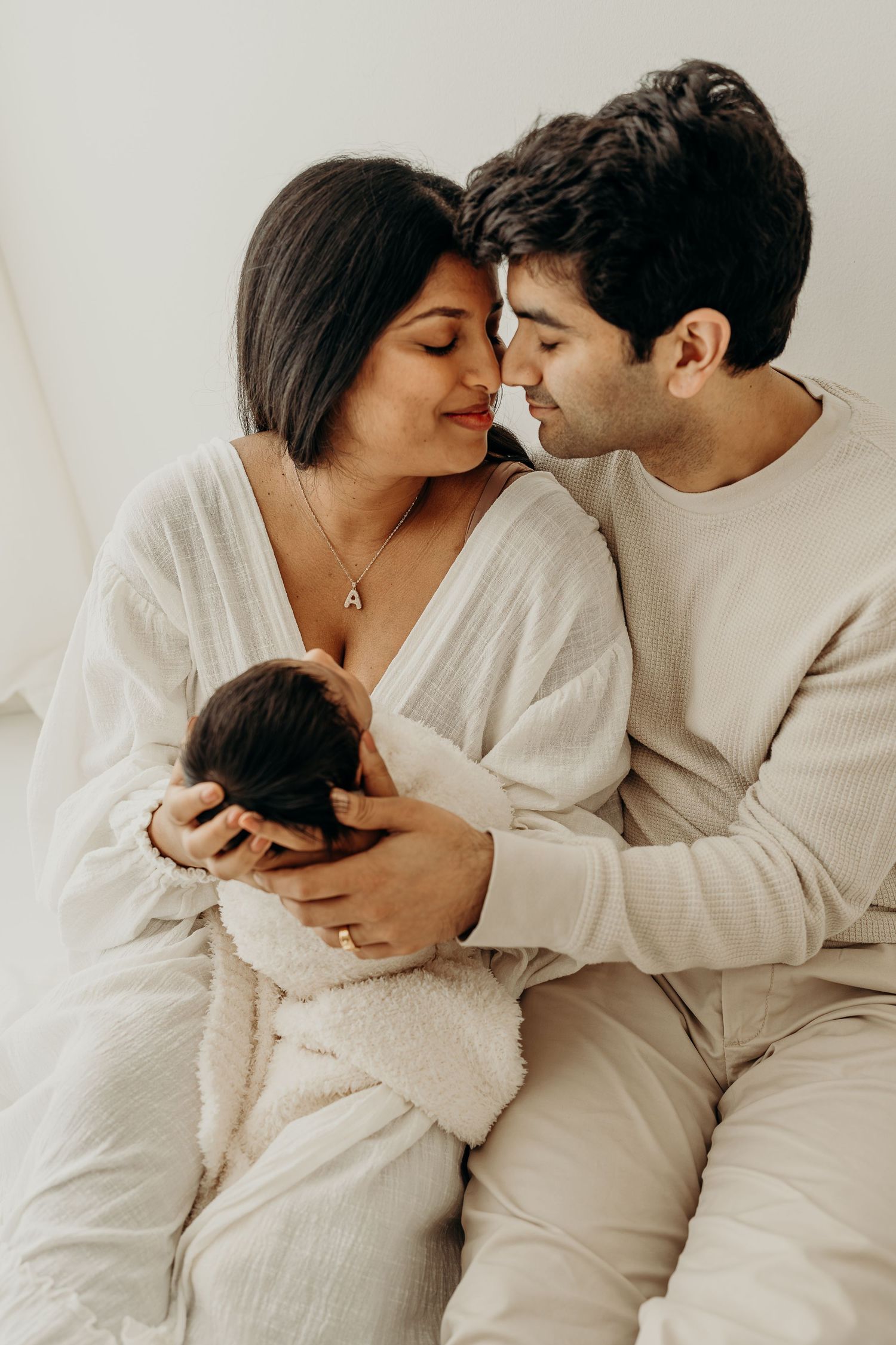 A couple in cream outfits tenderly holds their newborn baby, sharing an intimate moment together taken at Slatestudio, newborn studio