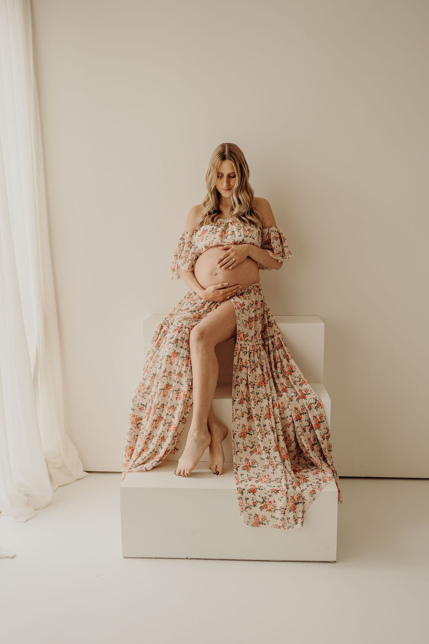 Artistic maternity photos in floral dress with dramatic poses on white platform.
